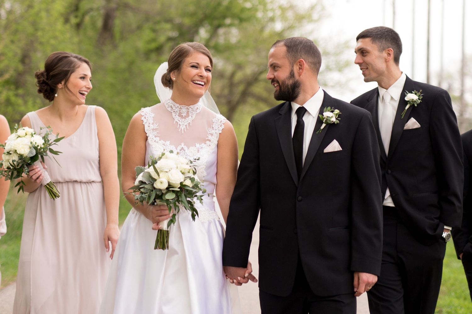 Wedding party outdoors smiling together while wearing formal attire with pink bridesmaids dress and black suits.