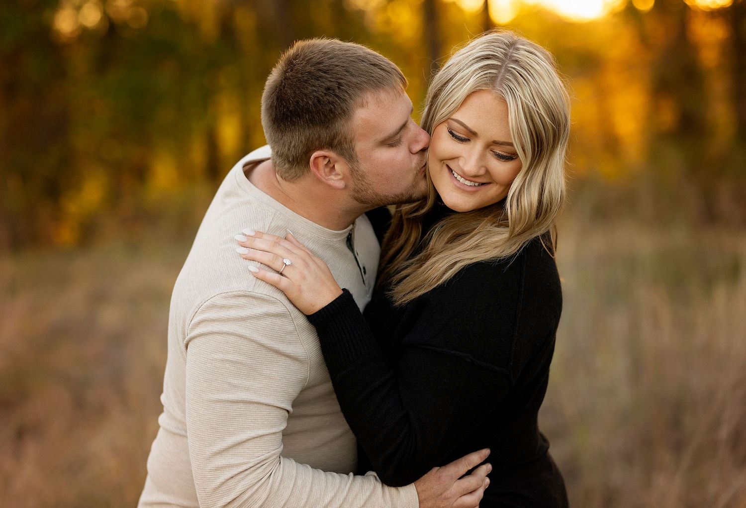 A romantic couple embraces during a sunset photoshoot in a golden field with warm autumn lighting.