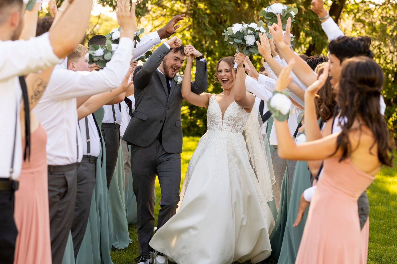 Wedding party celebrates outdoors as newlyweds walk through shower of flower petals in garden setting.