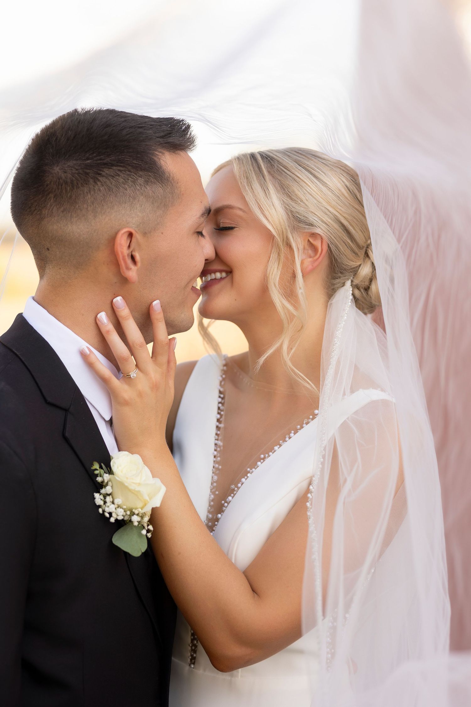 A romantic wedding photo showing a tender close-up of newlyweds sharing an intimate moment under a flowing veil.