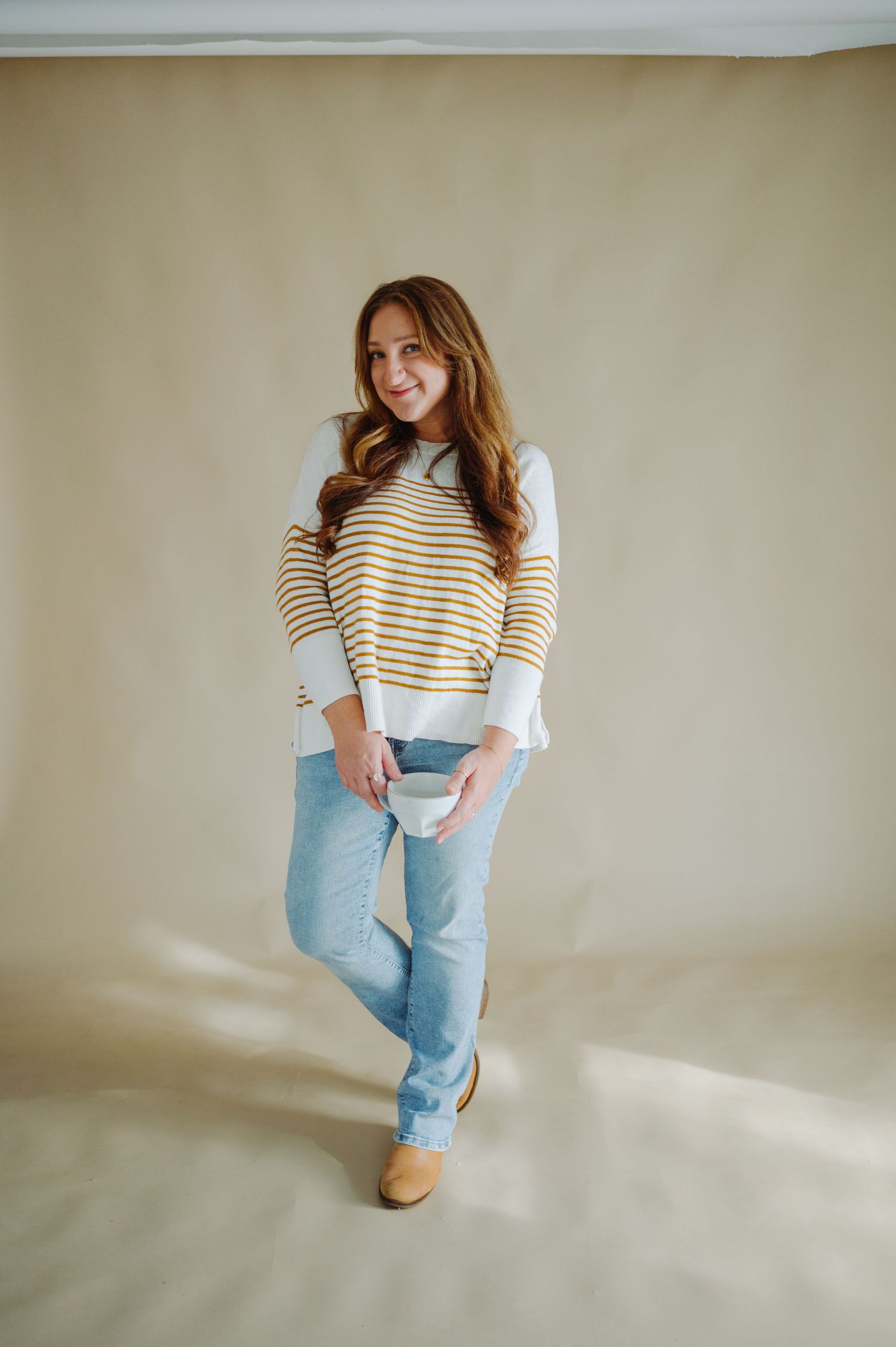A person poses in a striped sweater and light wash mom jeans against a neutral wall in multiple casual stances.