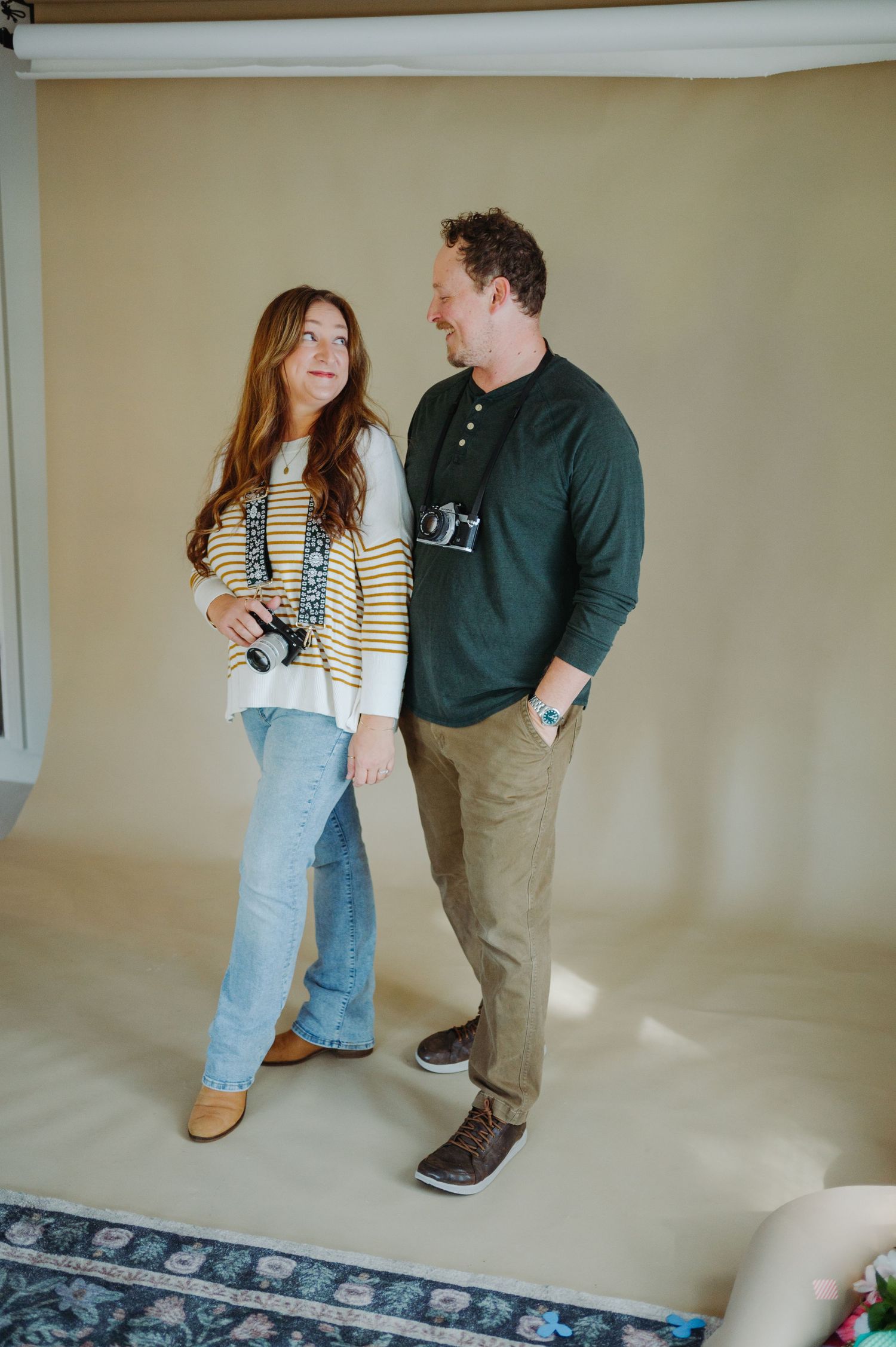 Two people stand in conversation on a light-colored floor in front of a beige wall.
