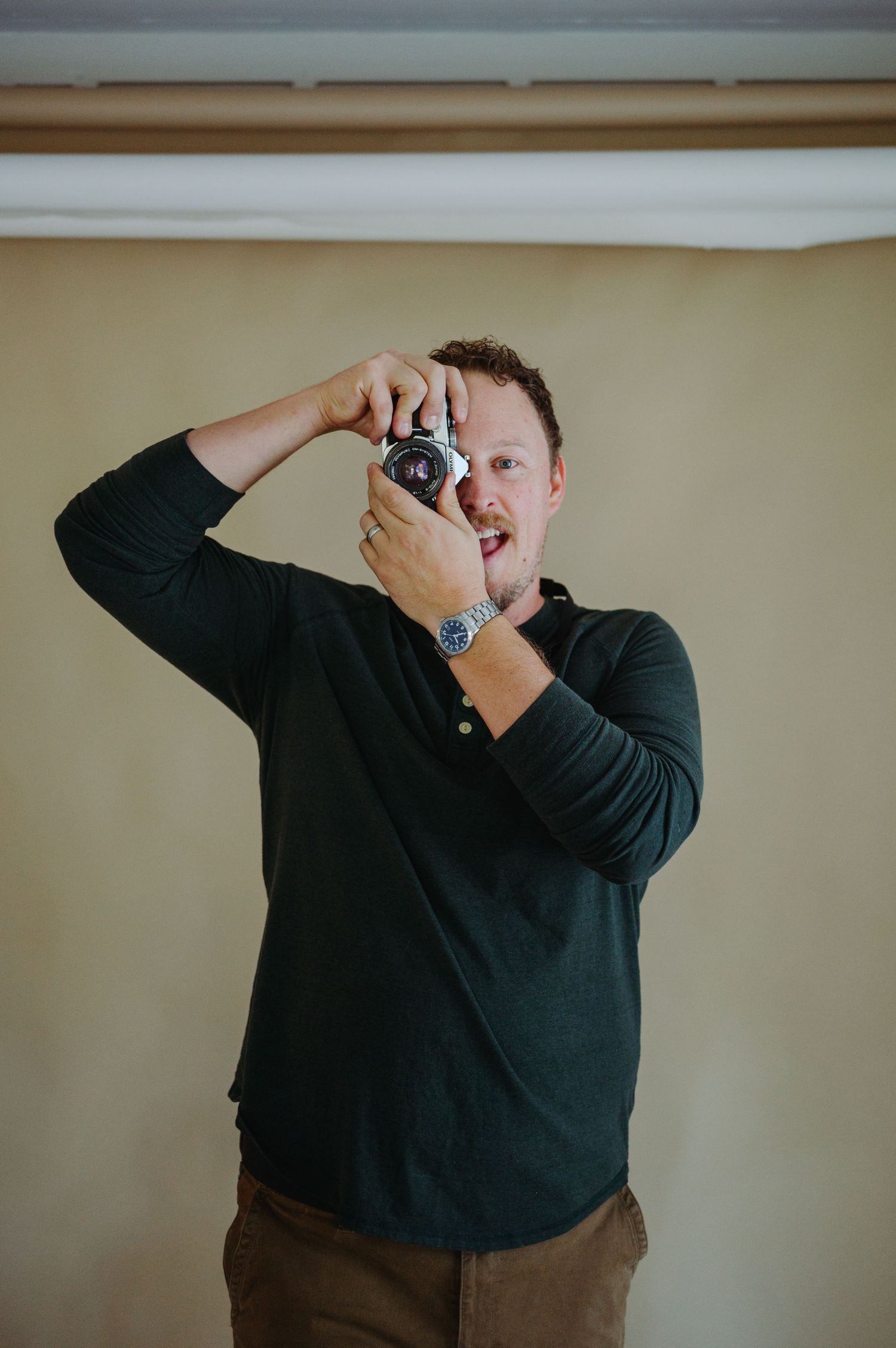 Person in black sweater holding vintage camera against neutral wall in sequential photography demonstration.