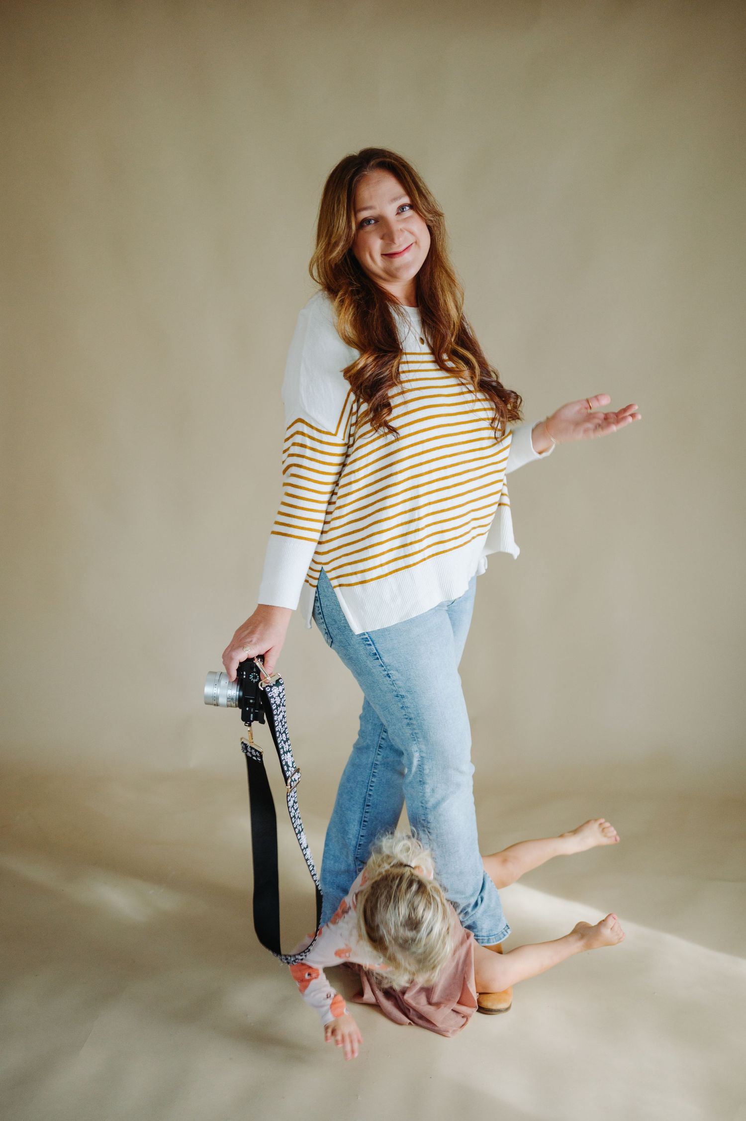 Woman in striped shirt and jeans poses playfully on beige background in studio setting.