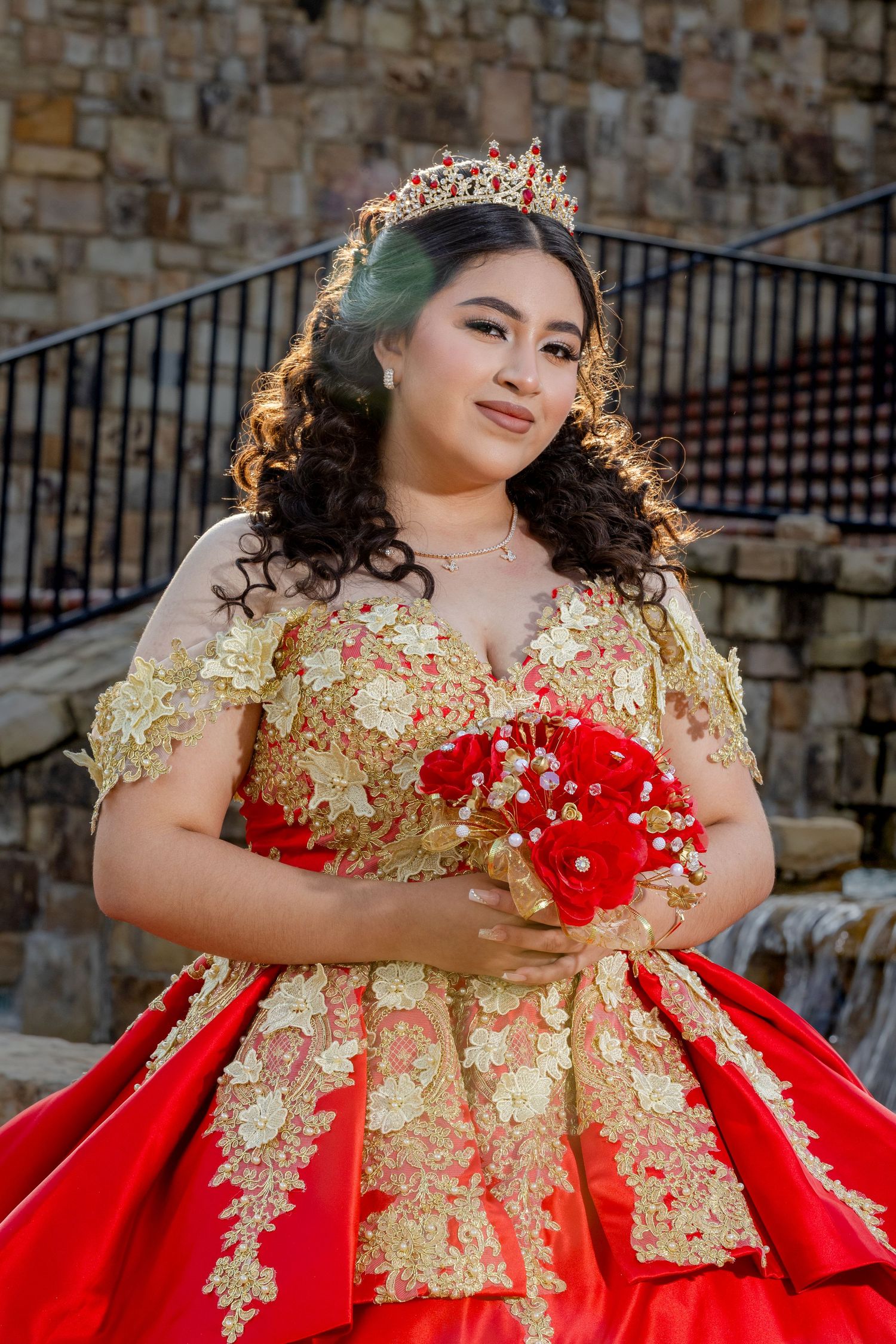 A close-up portrait showcasing an elaborate red and gold gown with crown and bouquet.
