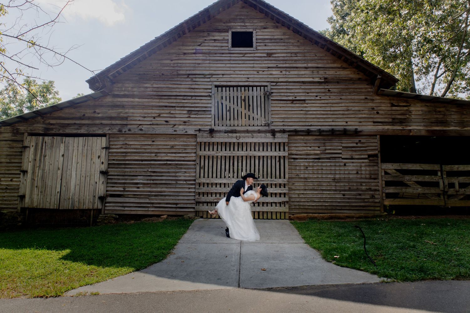 A romantic wedding photo in front of a rustic wooden barn with dramatic lighting.