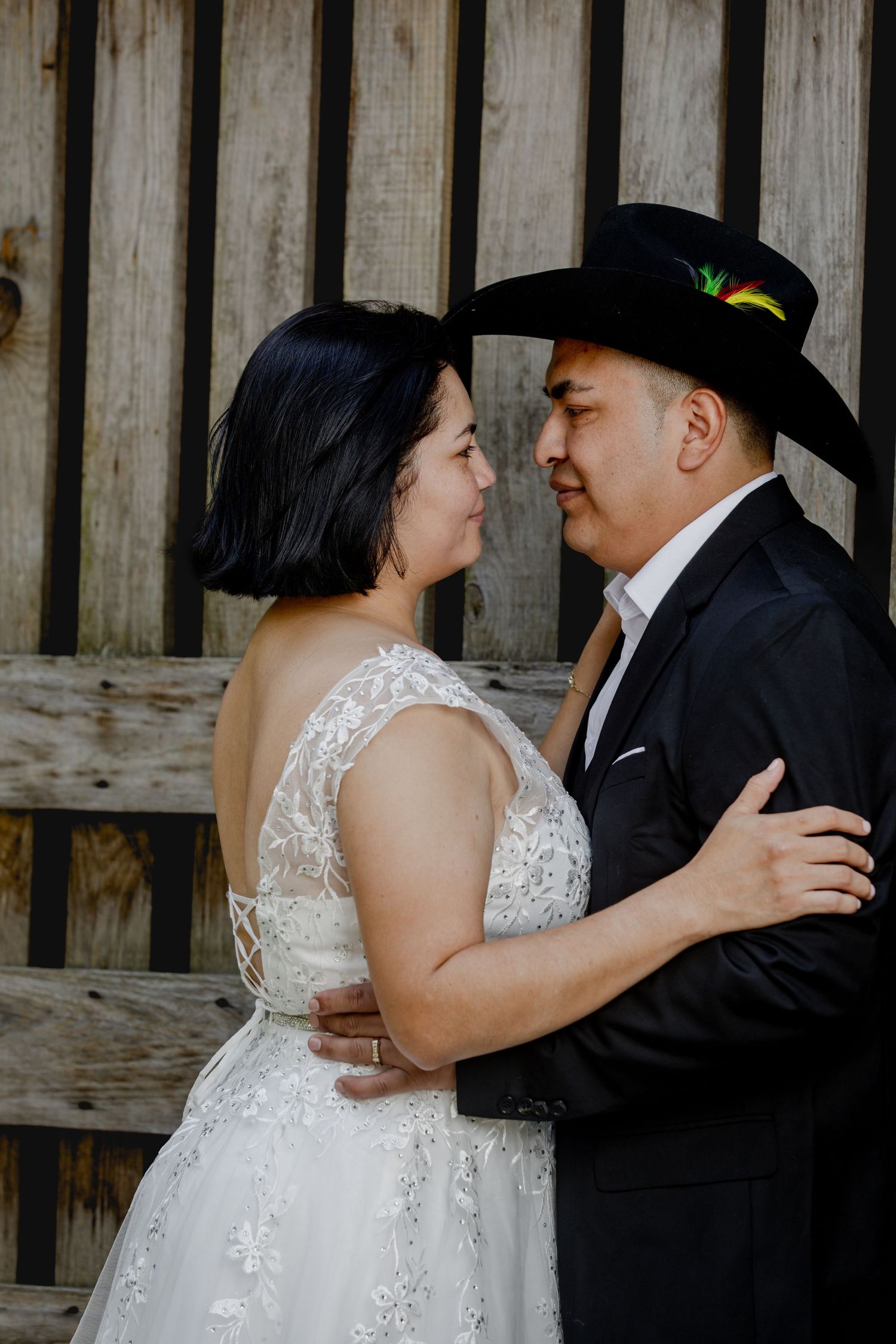 An intimate wedding portrait against rustic wooden walls with groom in black cowboy hat.