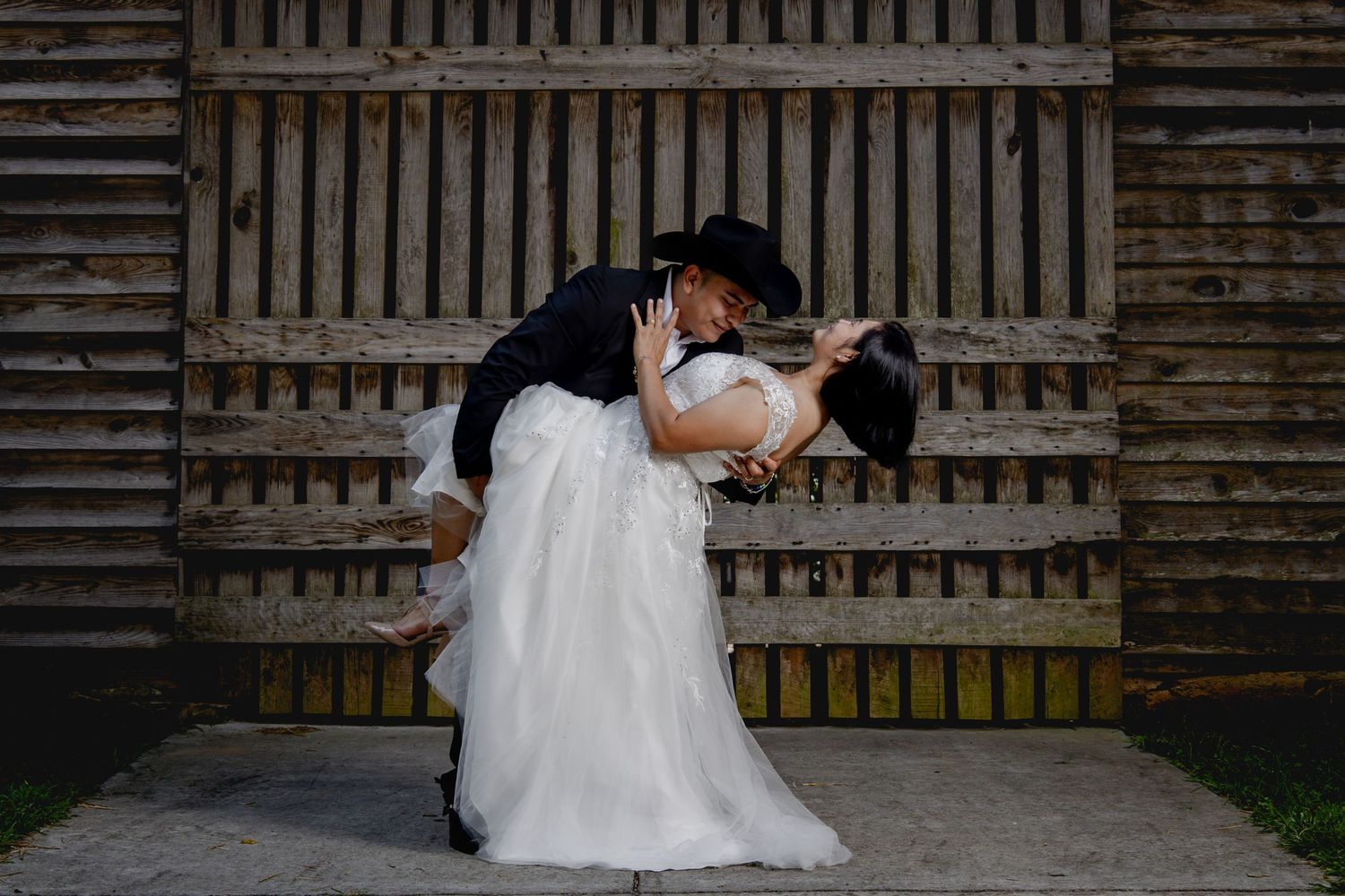 A romantic dip pose between newlyweds in front of a vintage wooden barn wall.