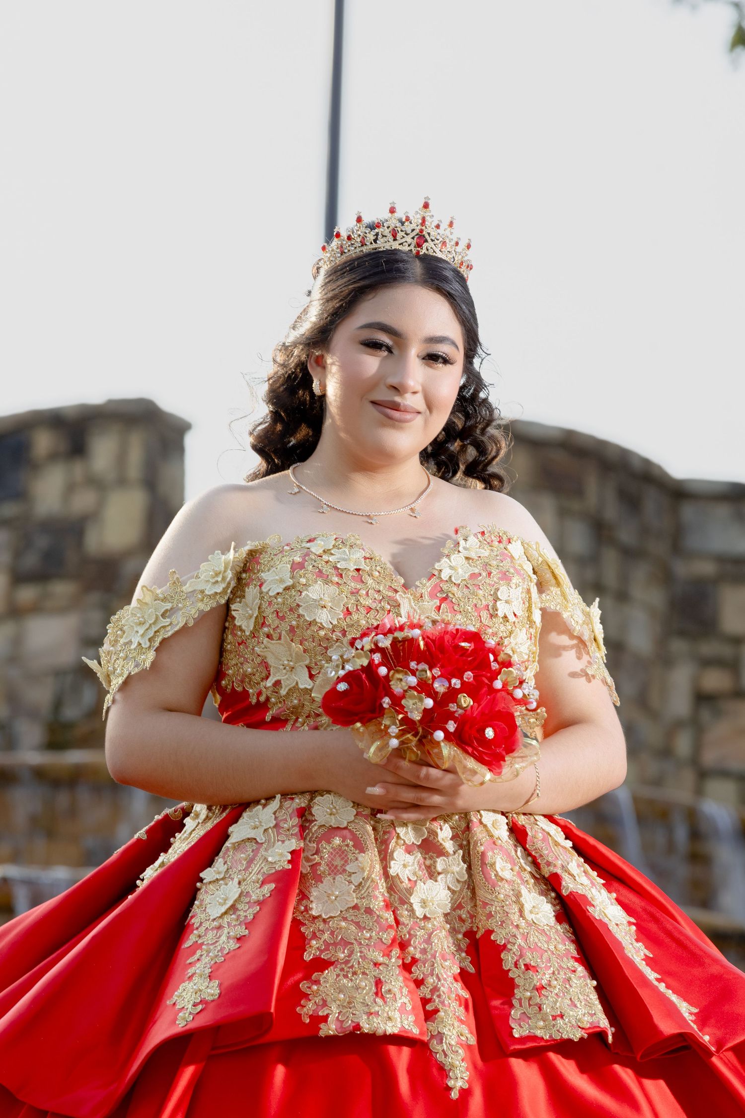 A detailed shot of an ornate red and gold ball gown with crown and red bouquet.
