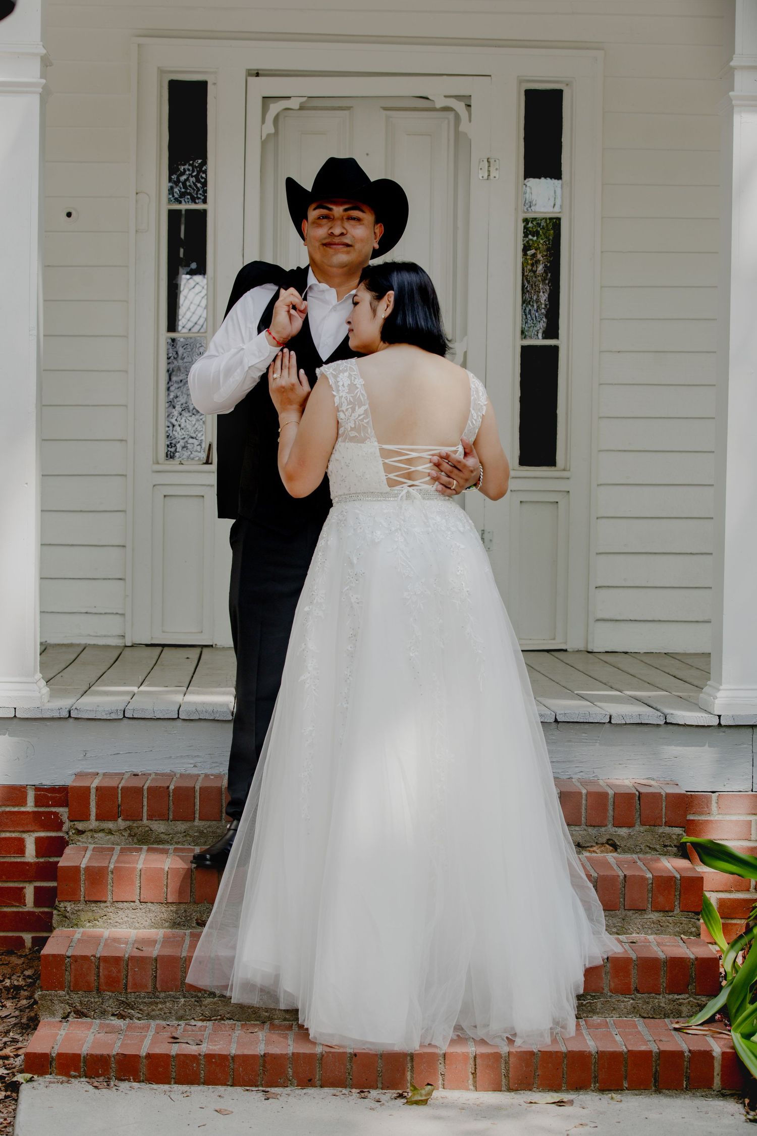 A couple shares a tender moment on a white porch with brick steps.