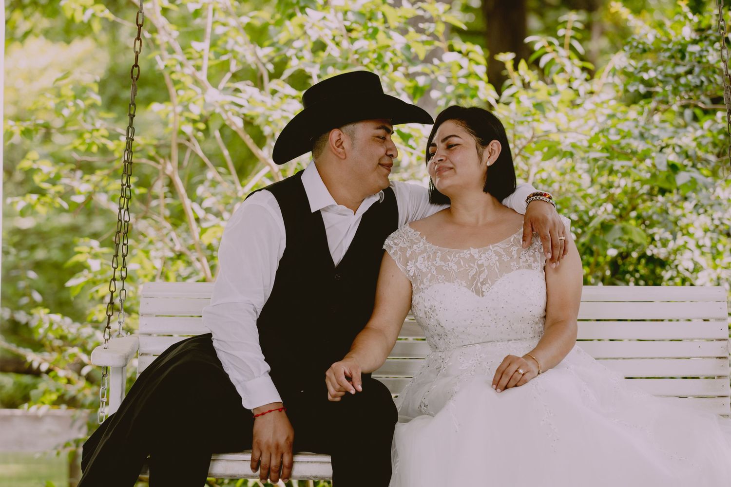 A romantic scene unfolds on a sunlit porch with greenery in the background.