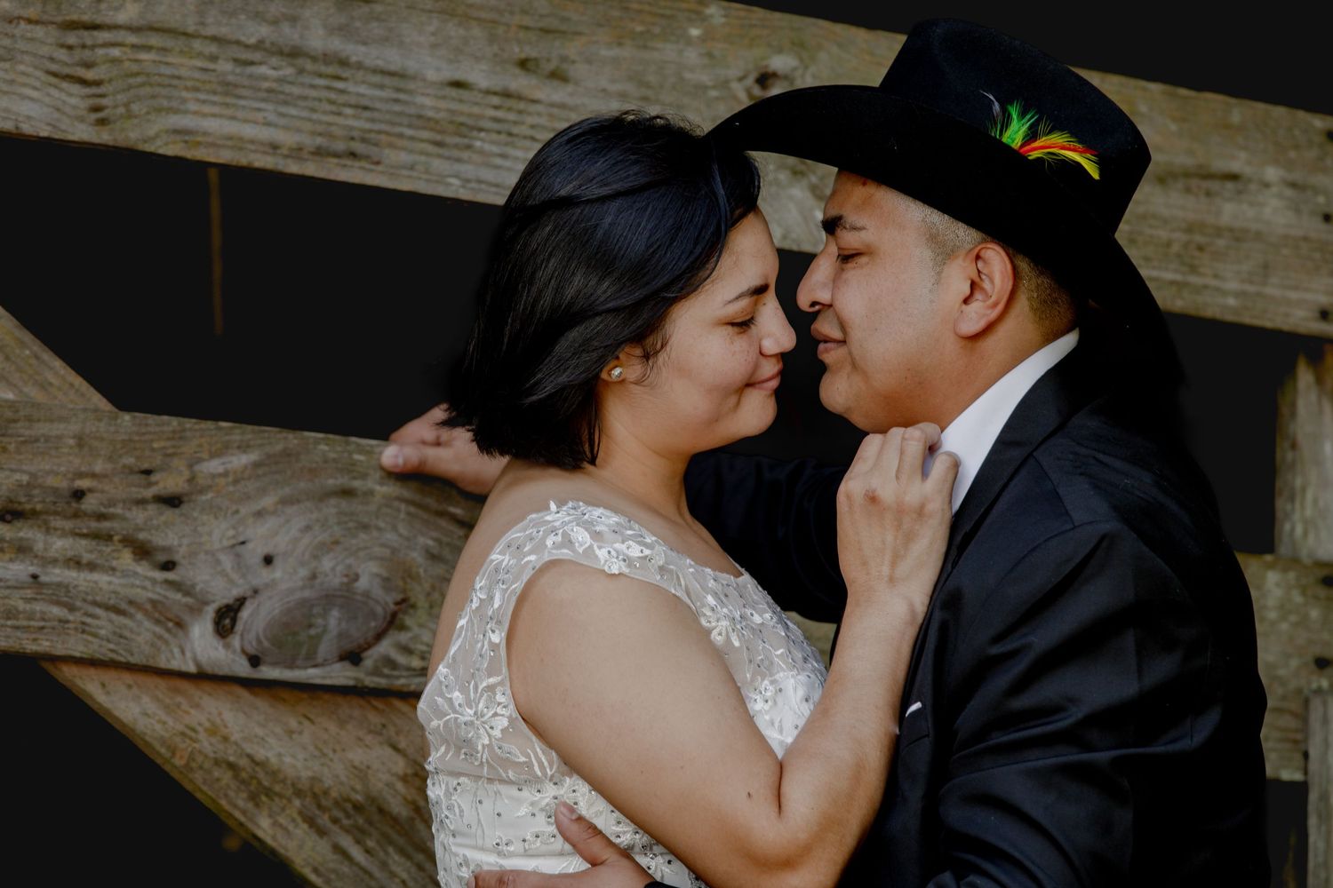 An intimate wedding portrait against weathered wood with groom in black cowboy hat.