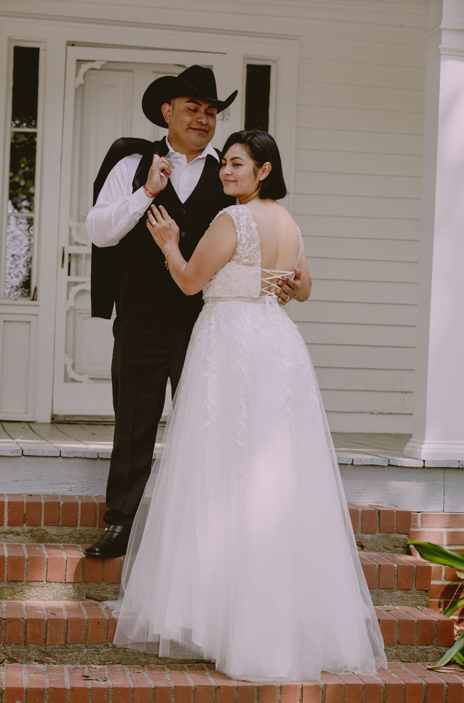 A couple shares intimate moments on a traditional white porch with brick steps.