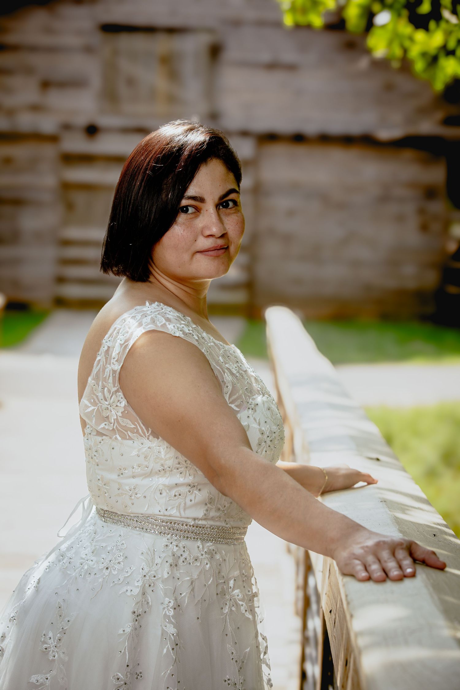 A bride poses gracefully in a beaded white wedding dress outdoors.