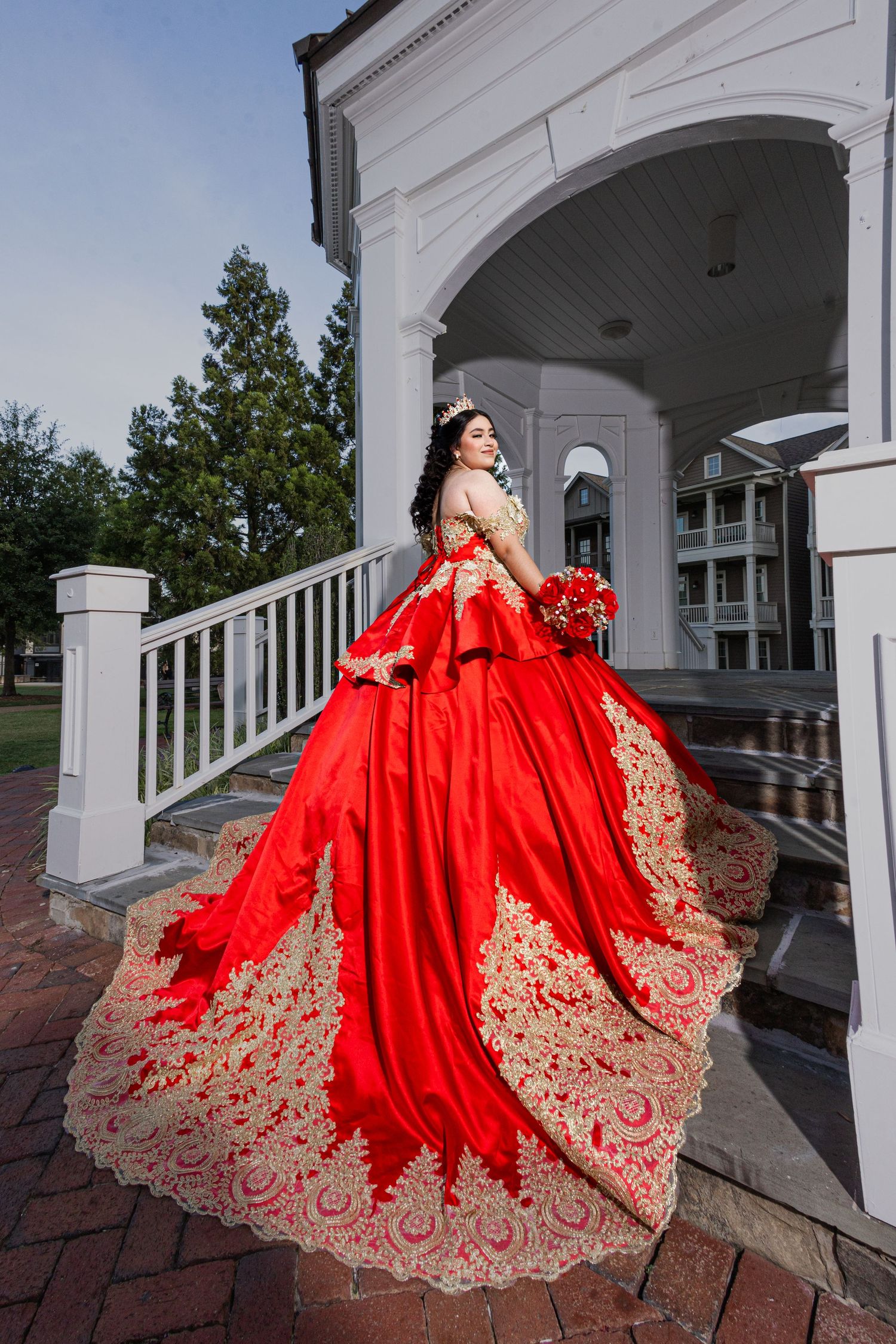 Dramatic red ball gown with gold lace details photographed at a classic white columned venue.