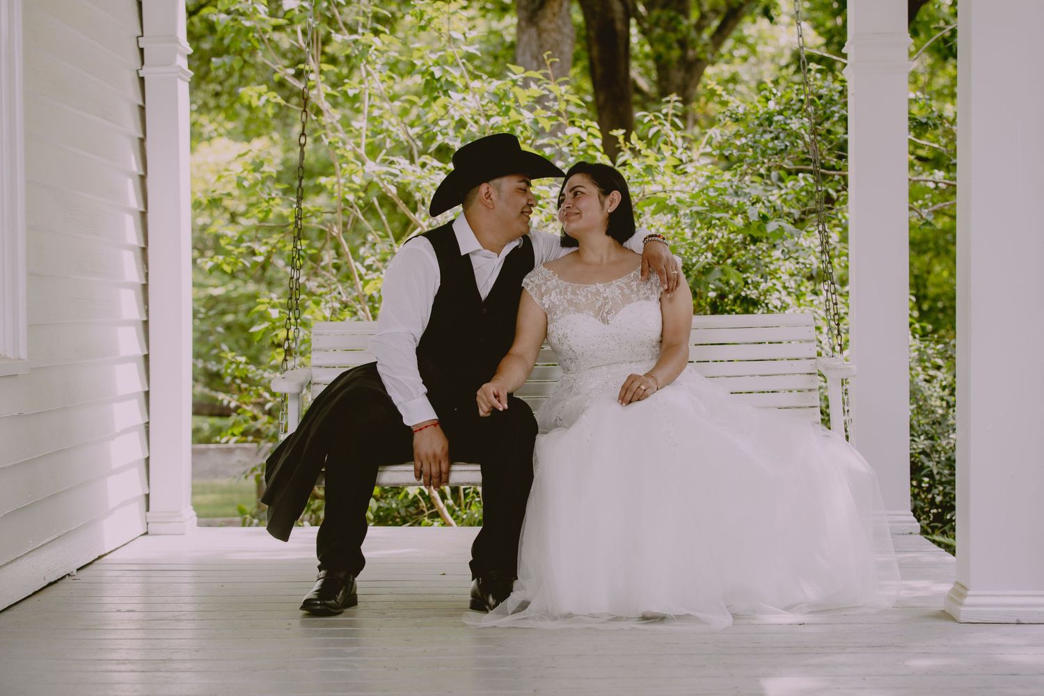 A couple shares tender moments on a white columned porch surrounded by greenery.