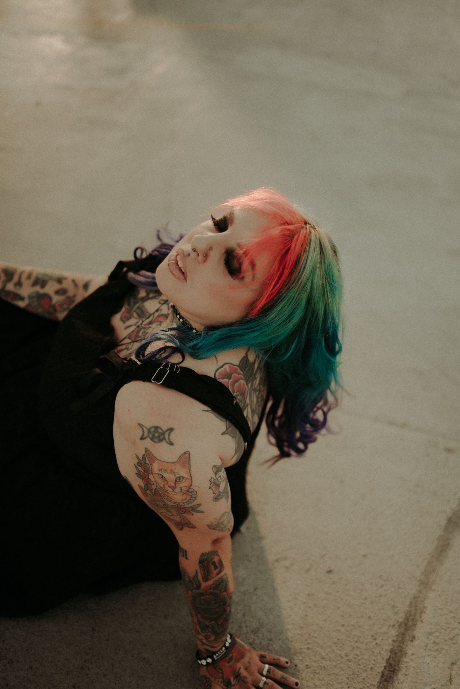 A person with colorful hair and tattoos lies on the ground in a series of artistic portrait photographs.