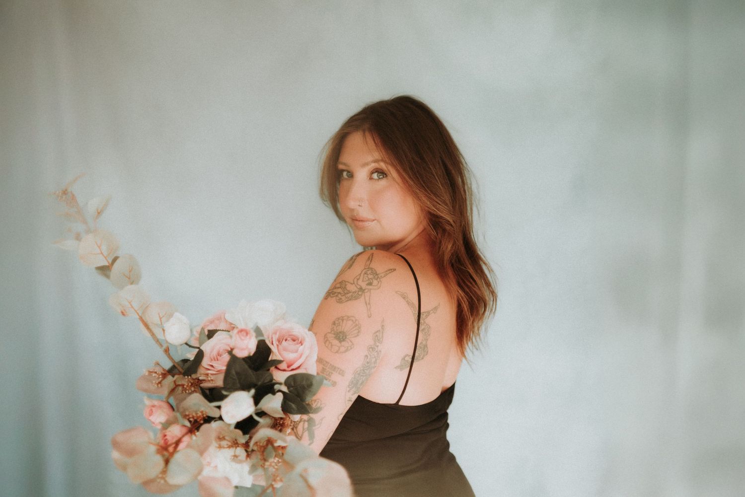 Person in a black dress holds a delicate floral arrangement against a soft, misty background.