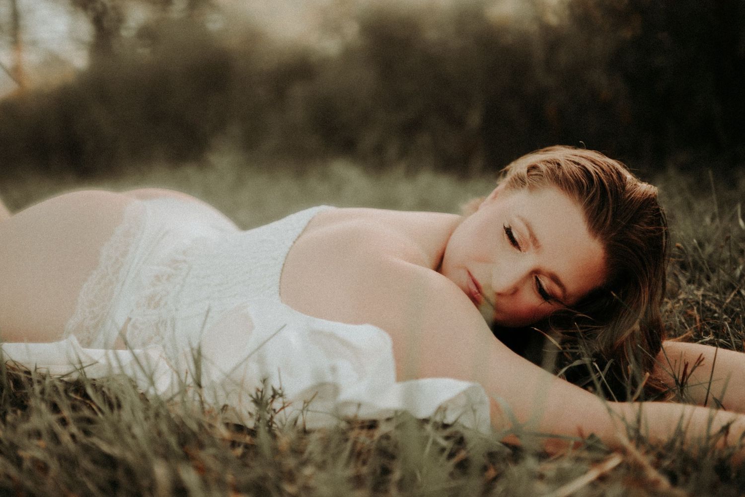 A person in a white dress lies peacefully in a grassy meadow during golden hour.