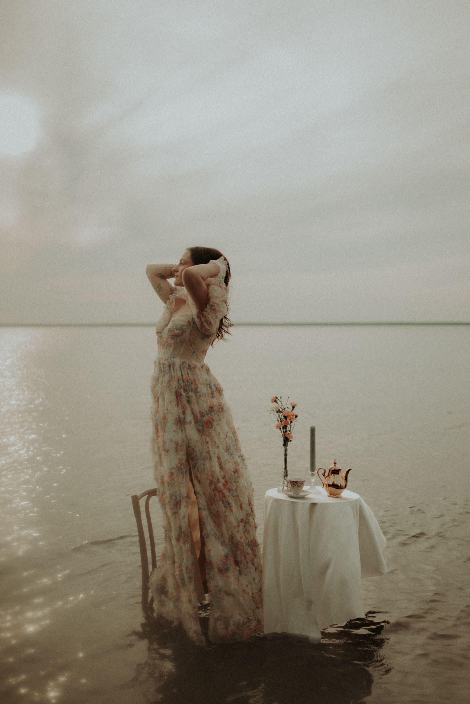 Artistic portrait in shallow waters with vintage dress and delicate table arrangement.