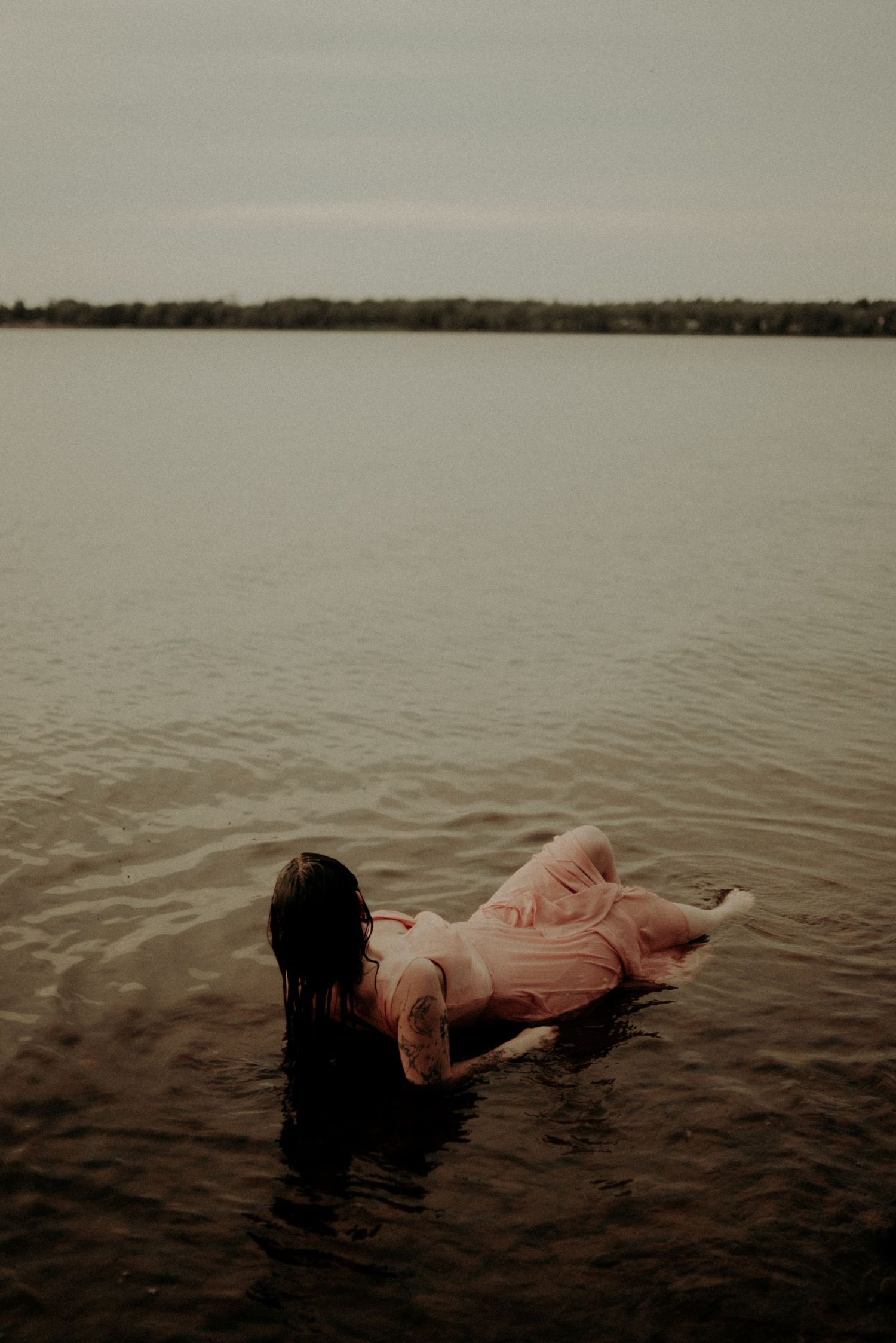 Serene water portrait showing a figure floating in a lake against a distant treeline.