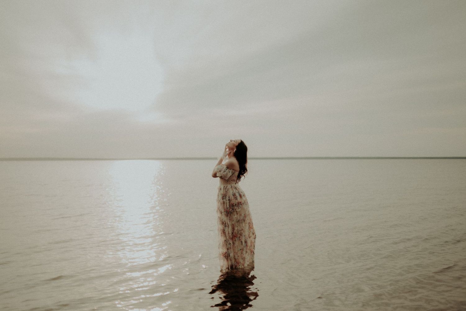 Moody water portrait featuring someone in vintage dress against overcast sky.