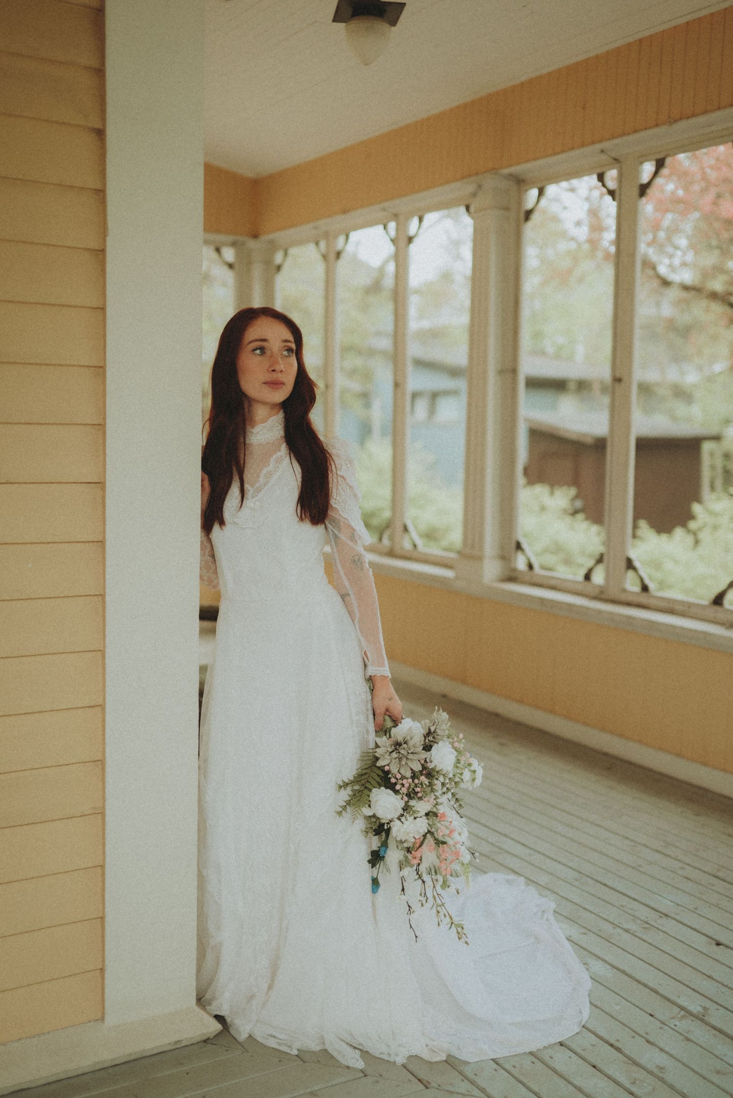 An elegant bridal portrait on a covered porch featuring a long-sleeved lace wedding gown and delicate bouquet.