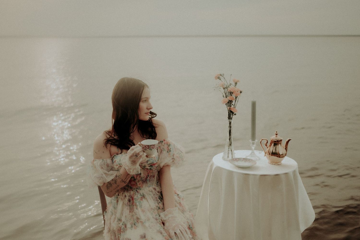 Artistic portrait of flowing dress against serene water backdrop with white table setting.