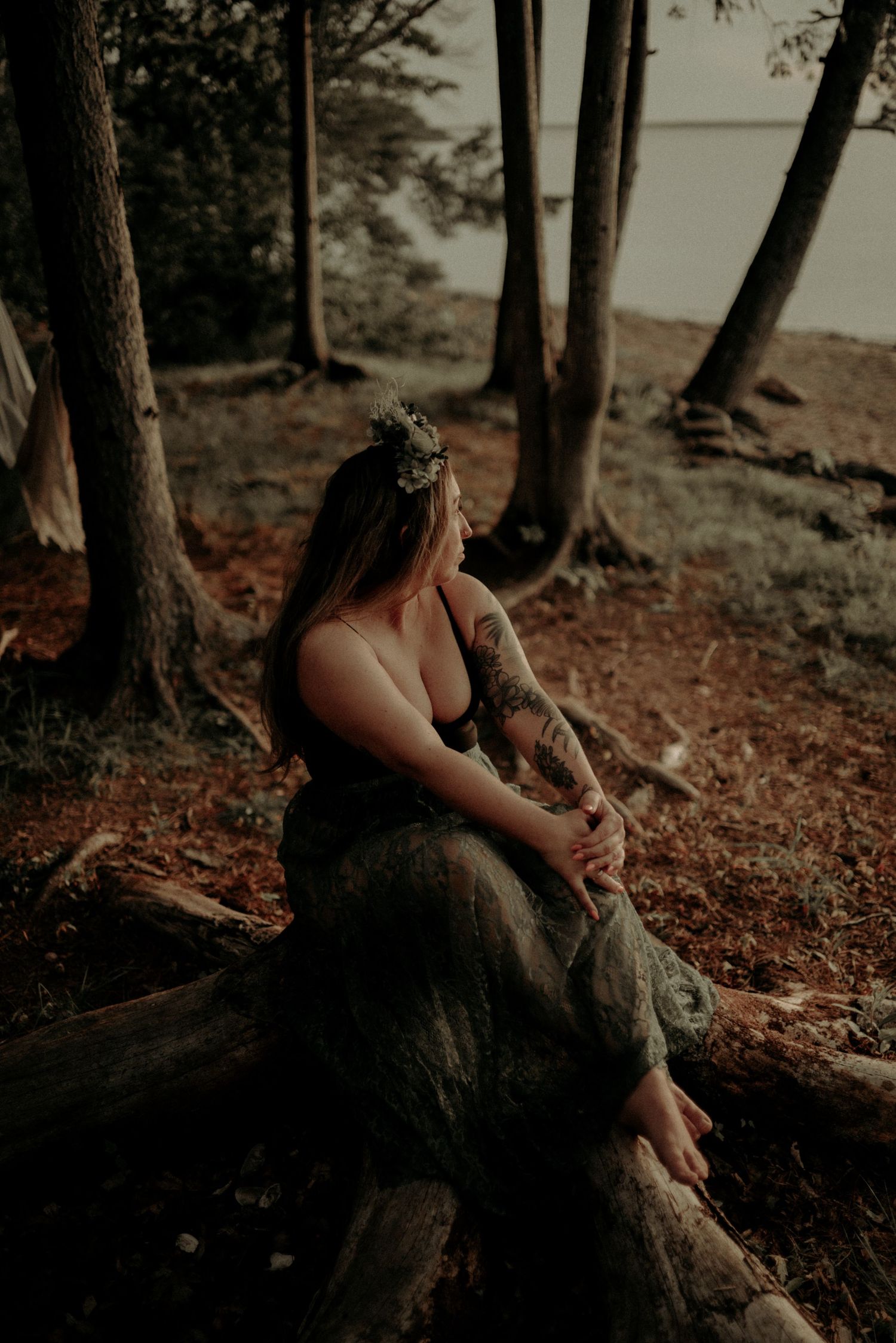 Moody woodland portrait with warm tones showing someone sitting on a fallen tree trunk near the shore.