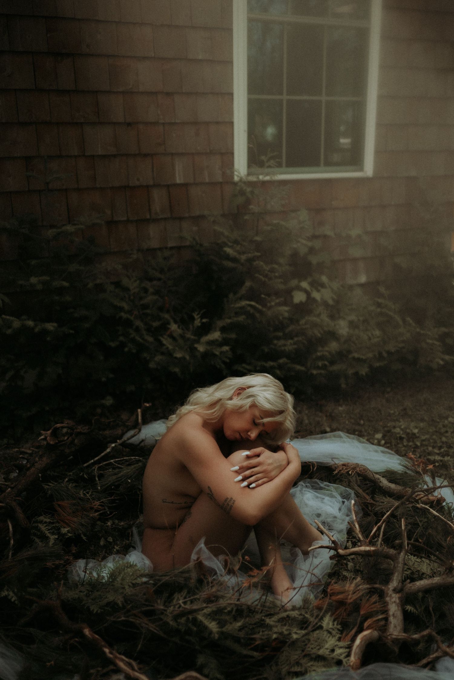 Artistic nude photography in natural outdoor setting with soft light filtering through.