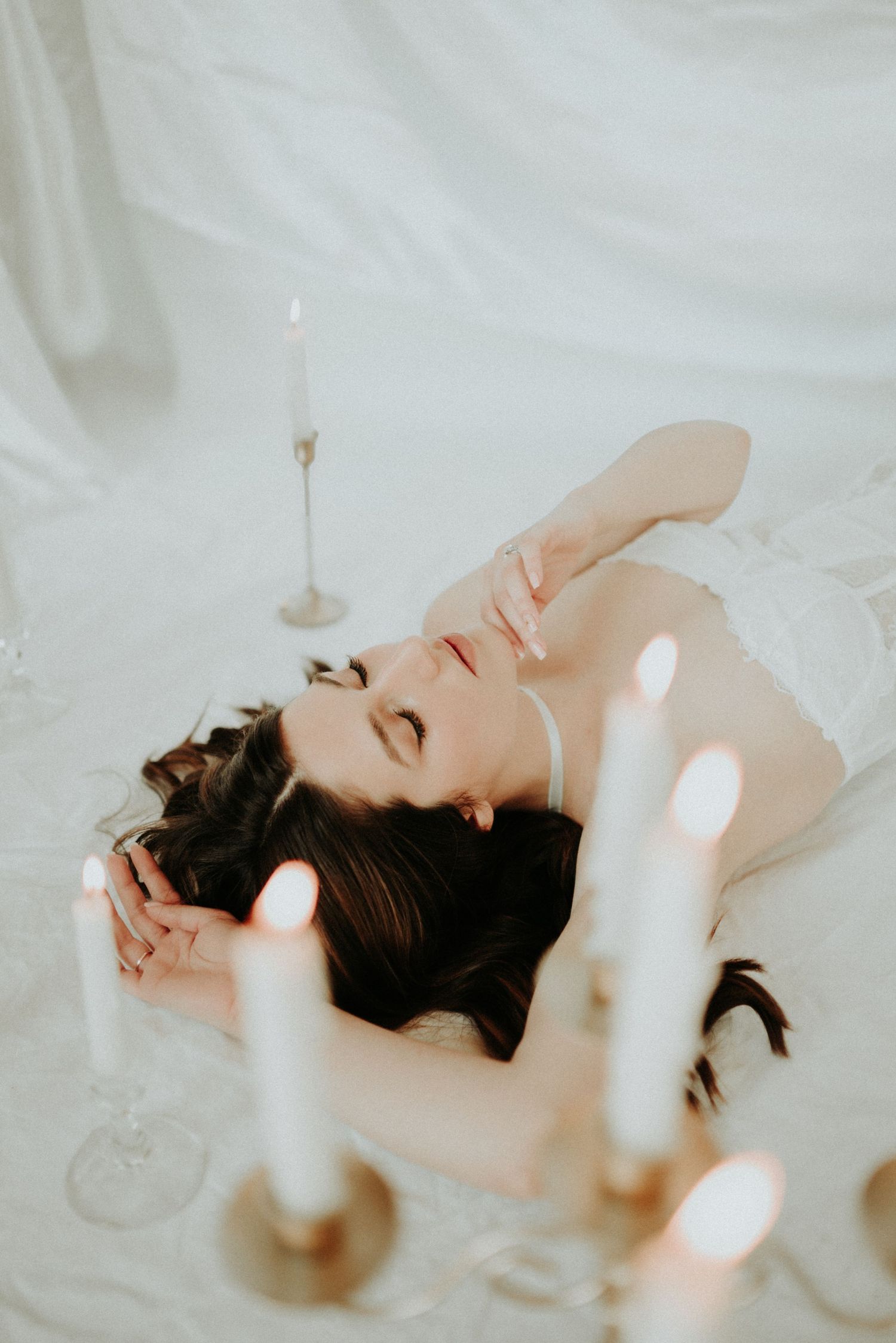 Dreamy boudoir photoshoot with candlelight creating soft glowing effects on white background.