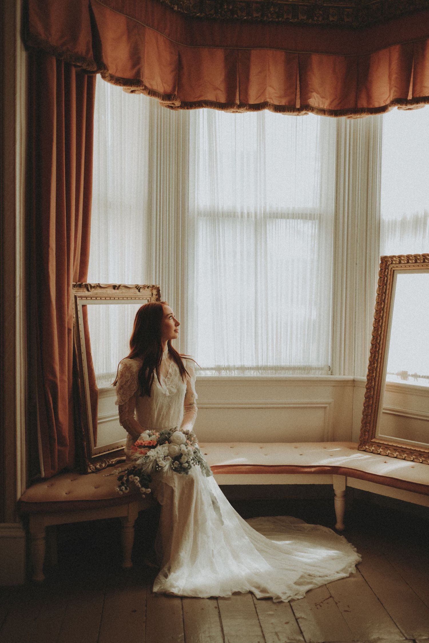 Artistic bridal portrait showcasing lace gown details against vintage window backdrop and warm lighting.