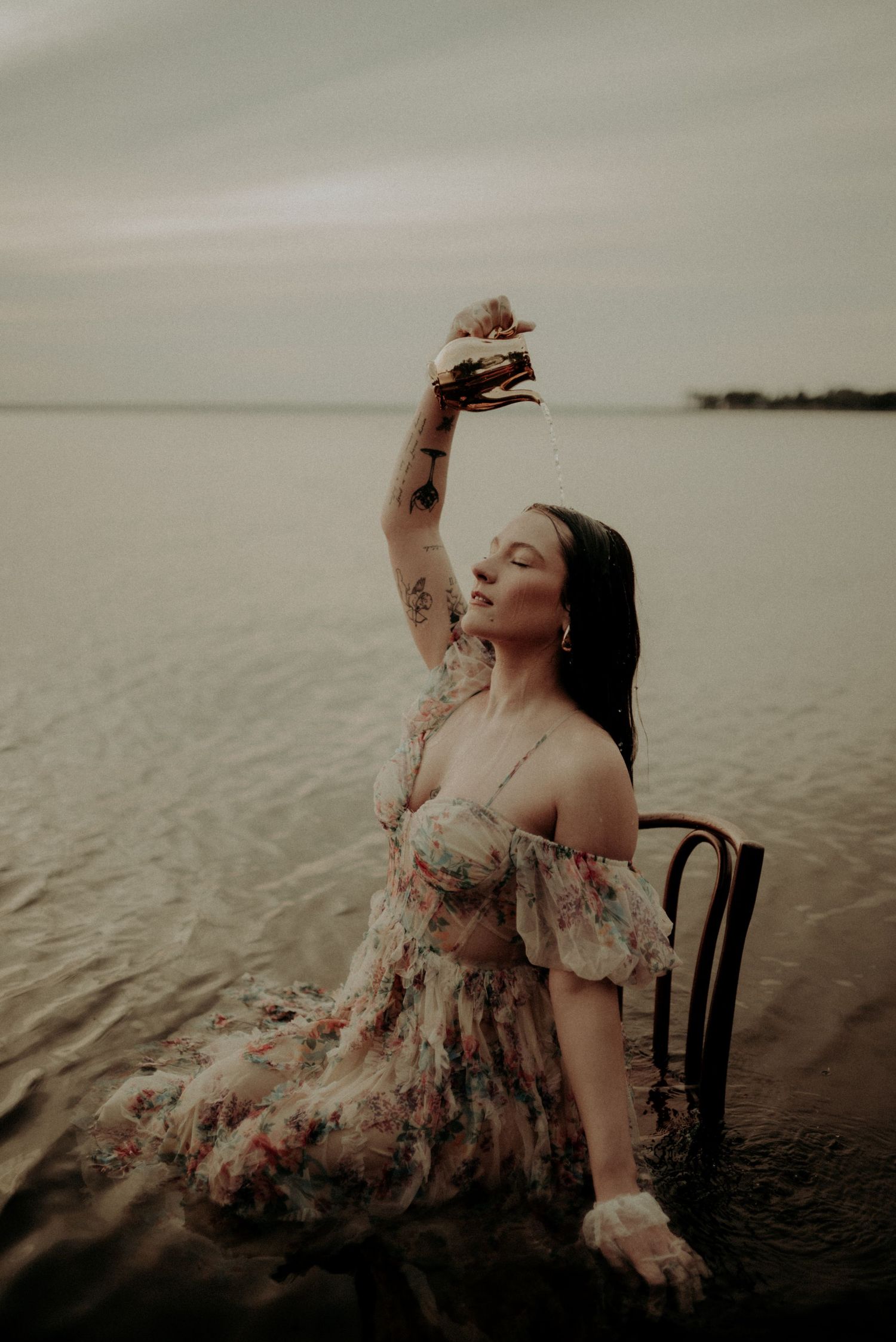 A dramatic portrait of someone in a floral dress holding a book while sitting in shallow water.