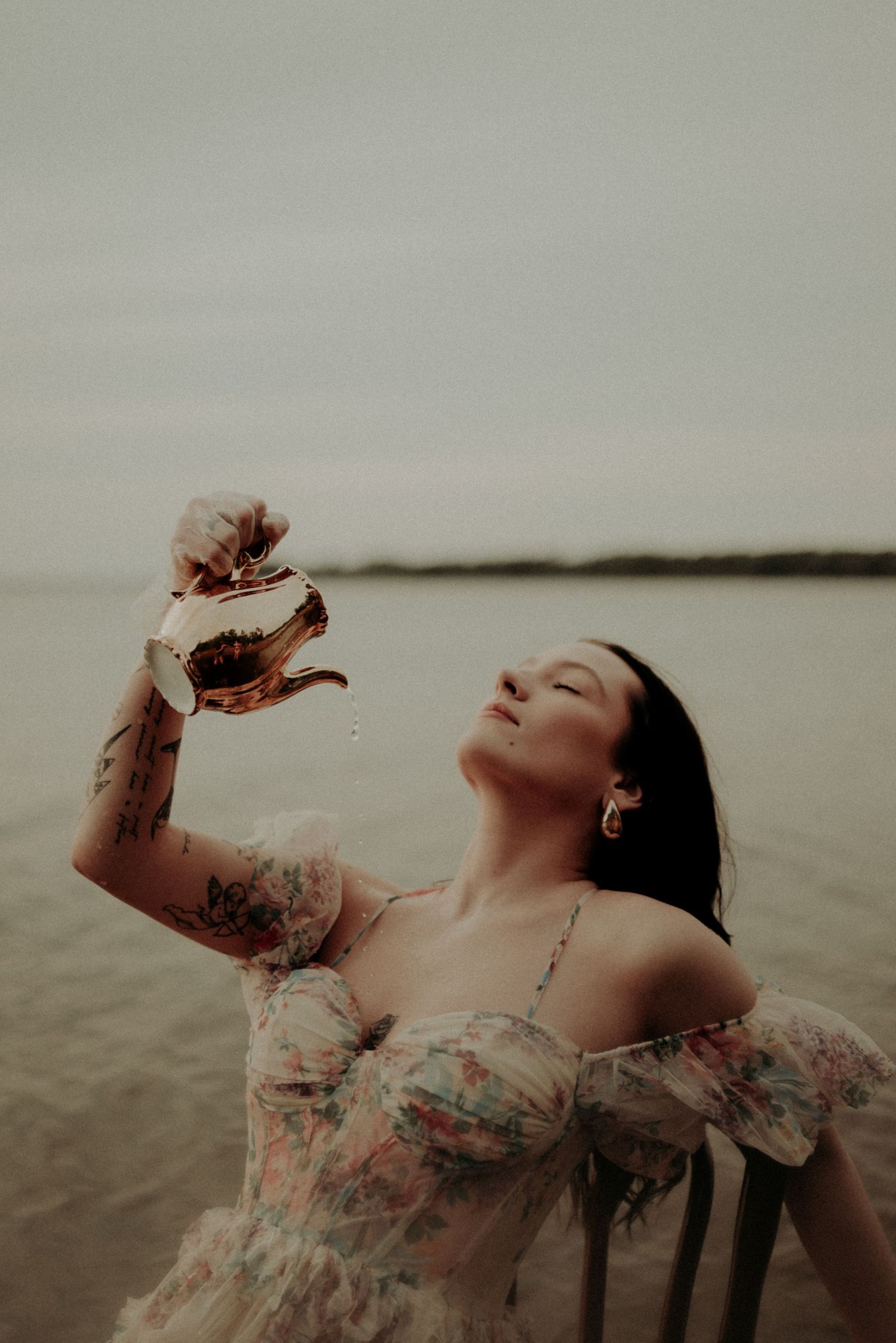 Dramatic portrait of someone in vintage dress reclining in shallow waters at dusk.
