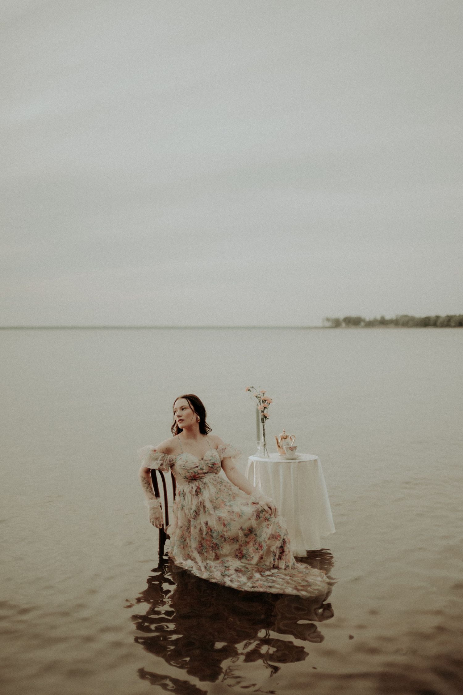 Vintage-inspired photoshoot with antique chair and table setting in calm waters at dusk.