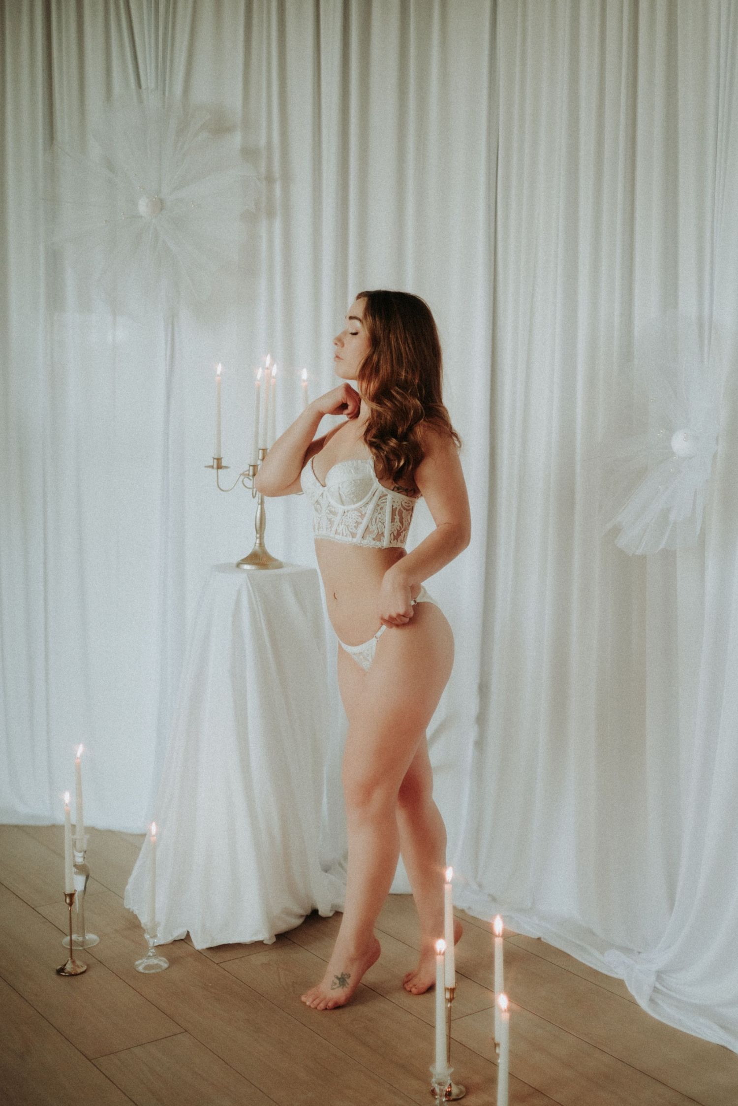 Ethereal boudoir scene with white curtains and lit candles creating romantic ambiance.