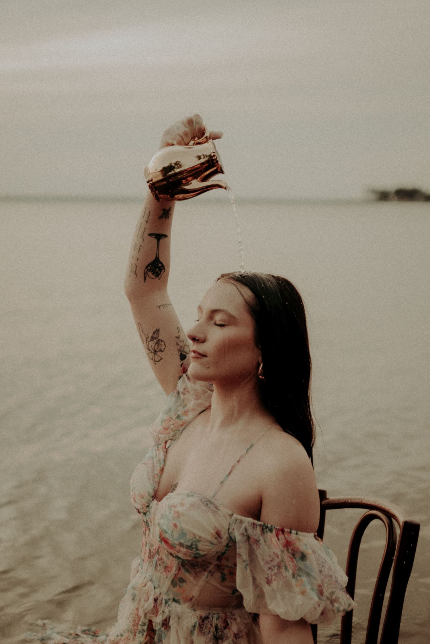 A moody portrait showing someone in an off-shoulder dress holding a book above their head in water.