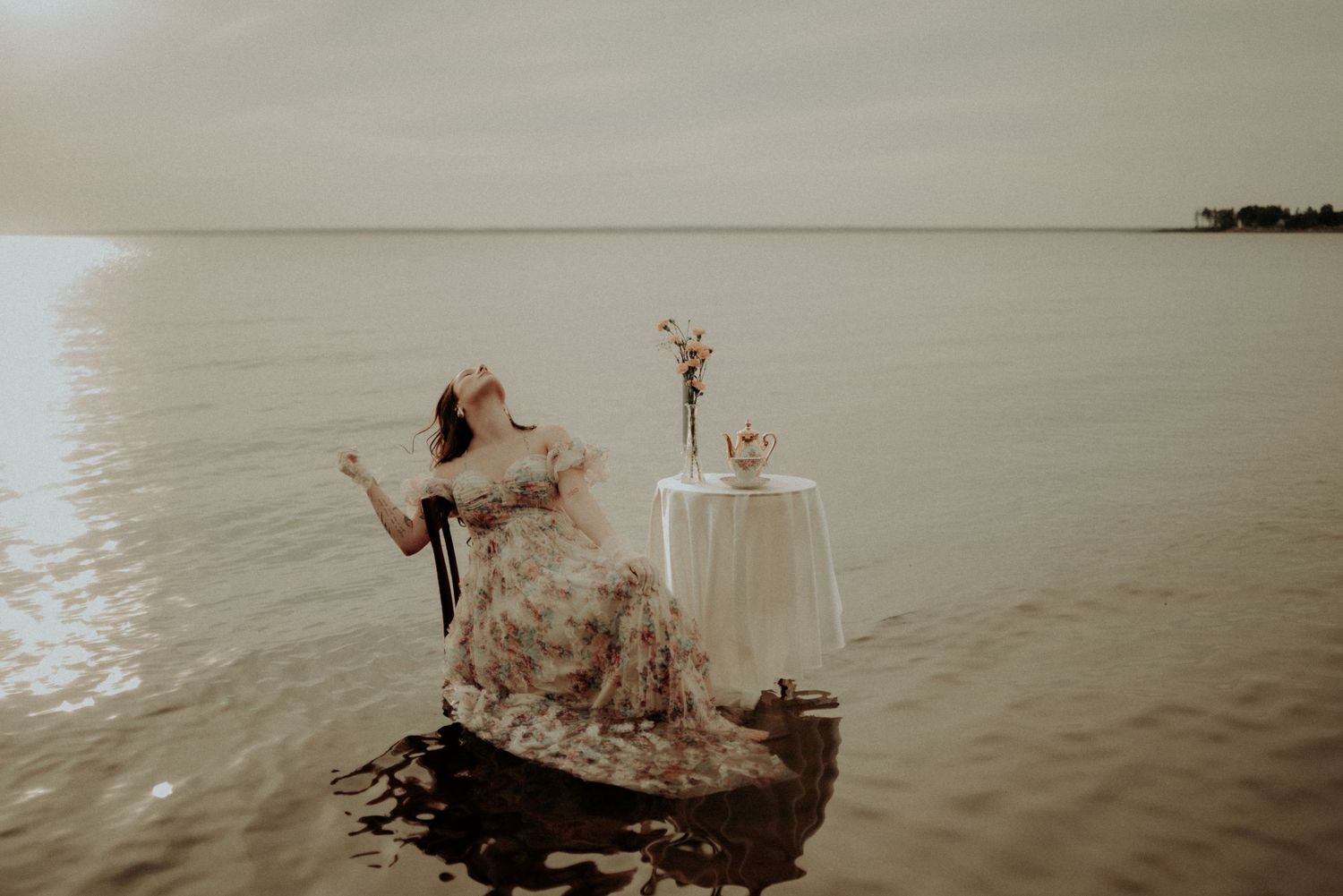 Dramatic water photography featuring flowing dress and vintage furniture in serene lake setting.