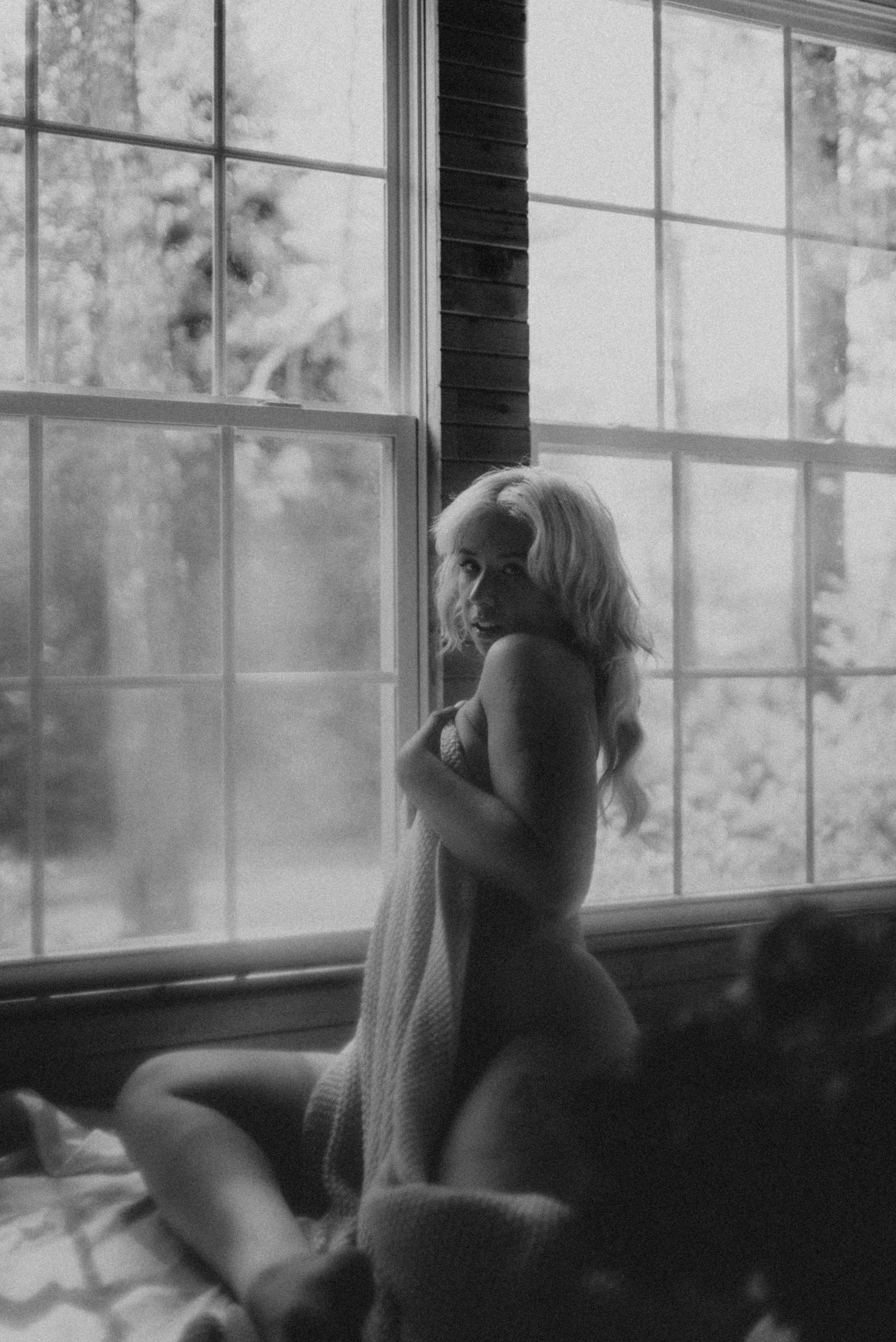 Vintage style black and white boudoir photo with dramatic window lighting.