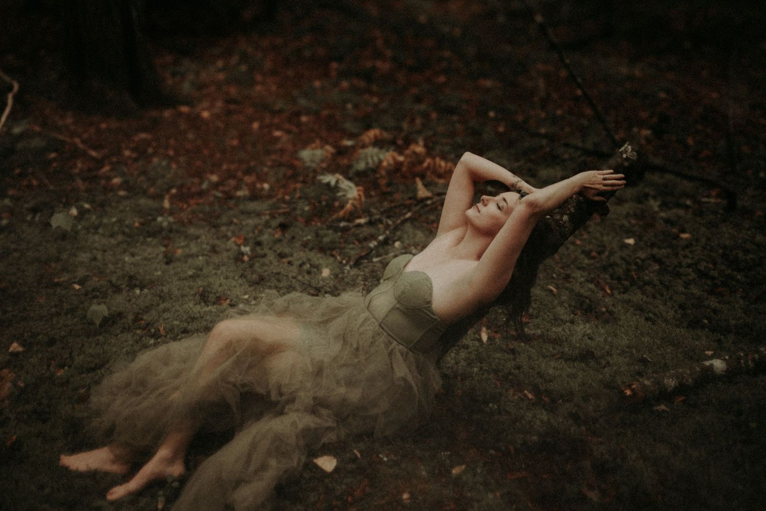 A dreamy forest photo with a flowing beige dress creating movement against fallen autumn leaves.