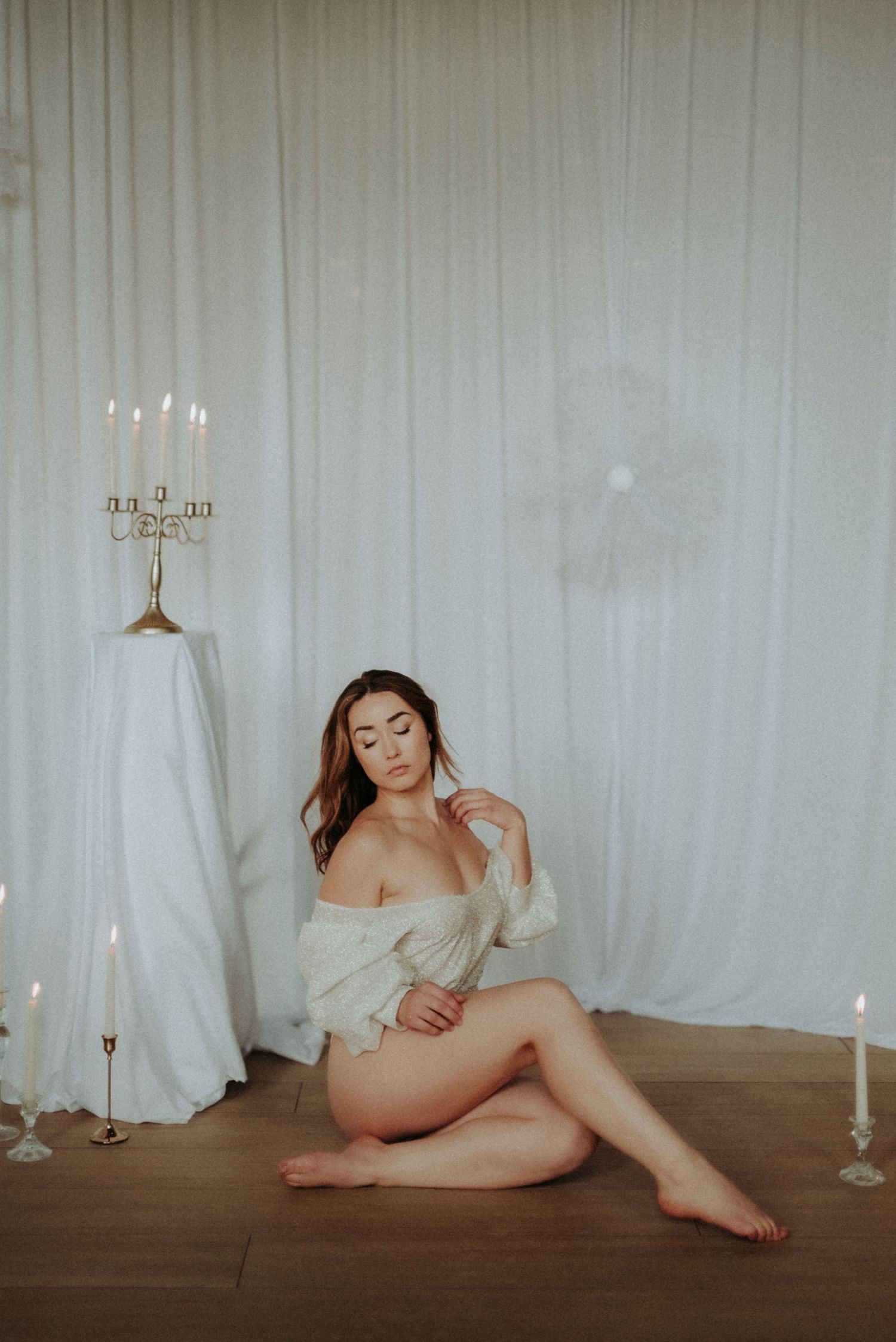 Ethereal boudoir photography with white fabric backdrop and glowing candles creating romantic ambiance.