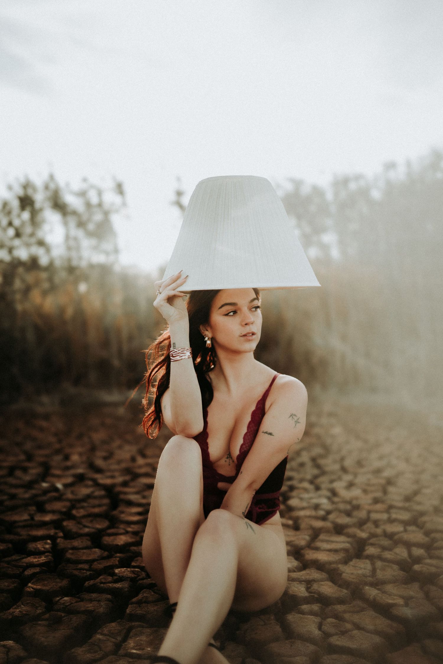 Artistic portrait series of a woman in a white hat sitting on cracked earth during golden hour sunset.