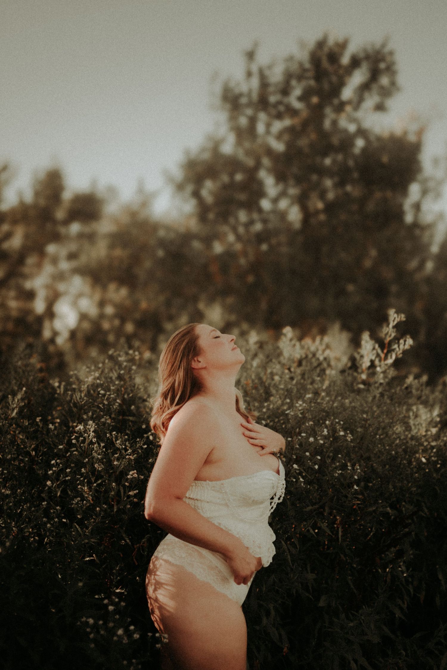 A figure stands in a sunlit field wearing a white dress with backlit wildflowers creating a dreamy golden atmosphere.