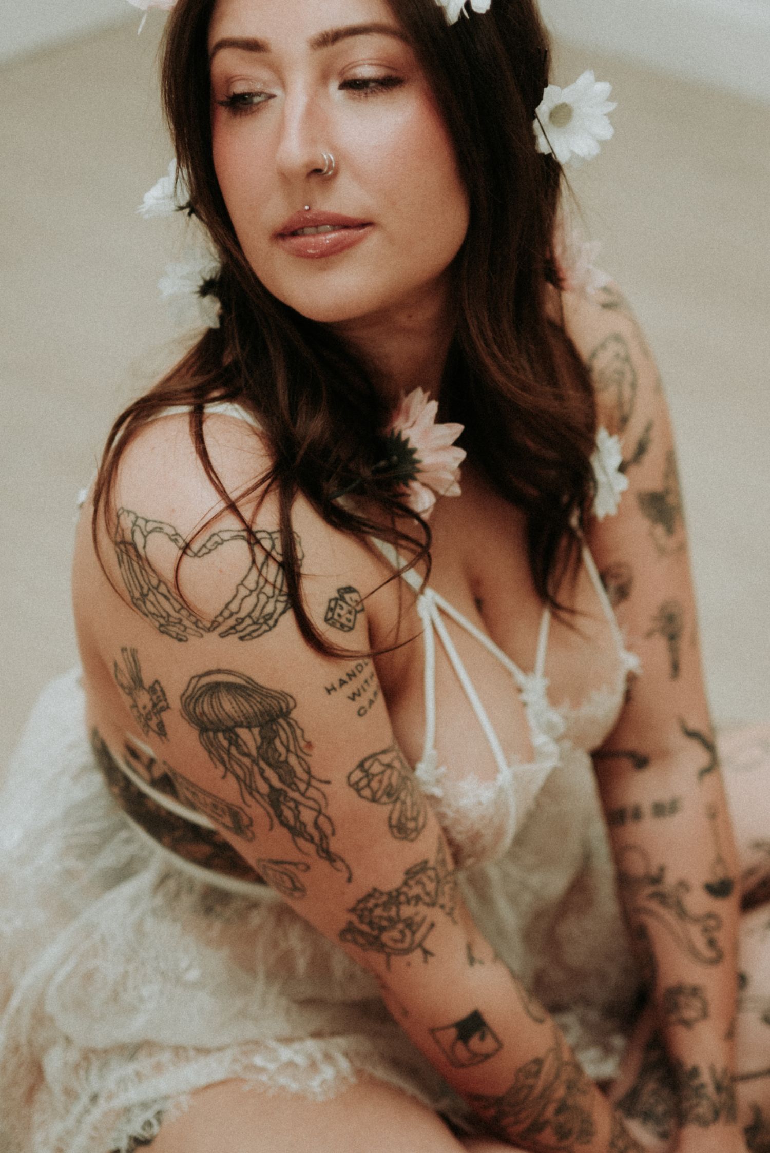 Artistic boudoir photo of person in white lingerie with visible tattoos in soft natural lighting.