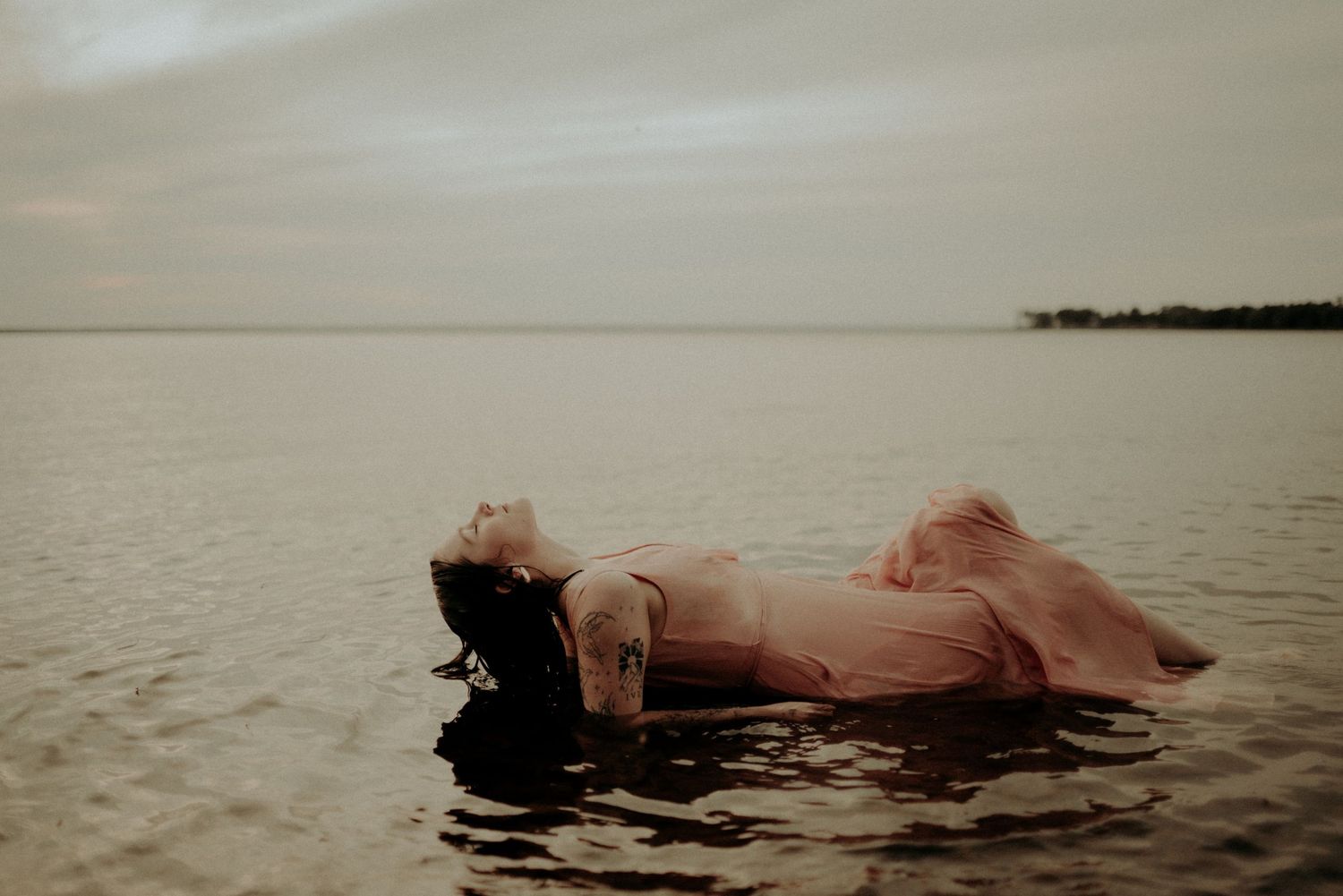 A tranquil water photoshoot featuring a person floating serenely in shallow waters at dusk.