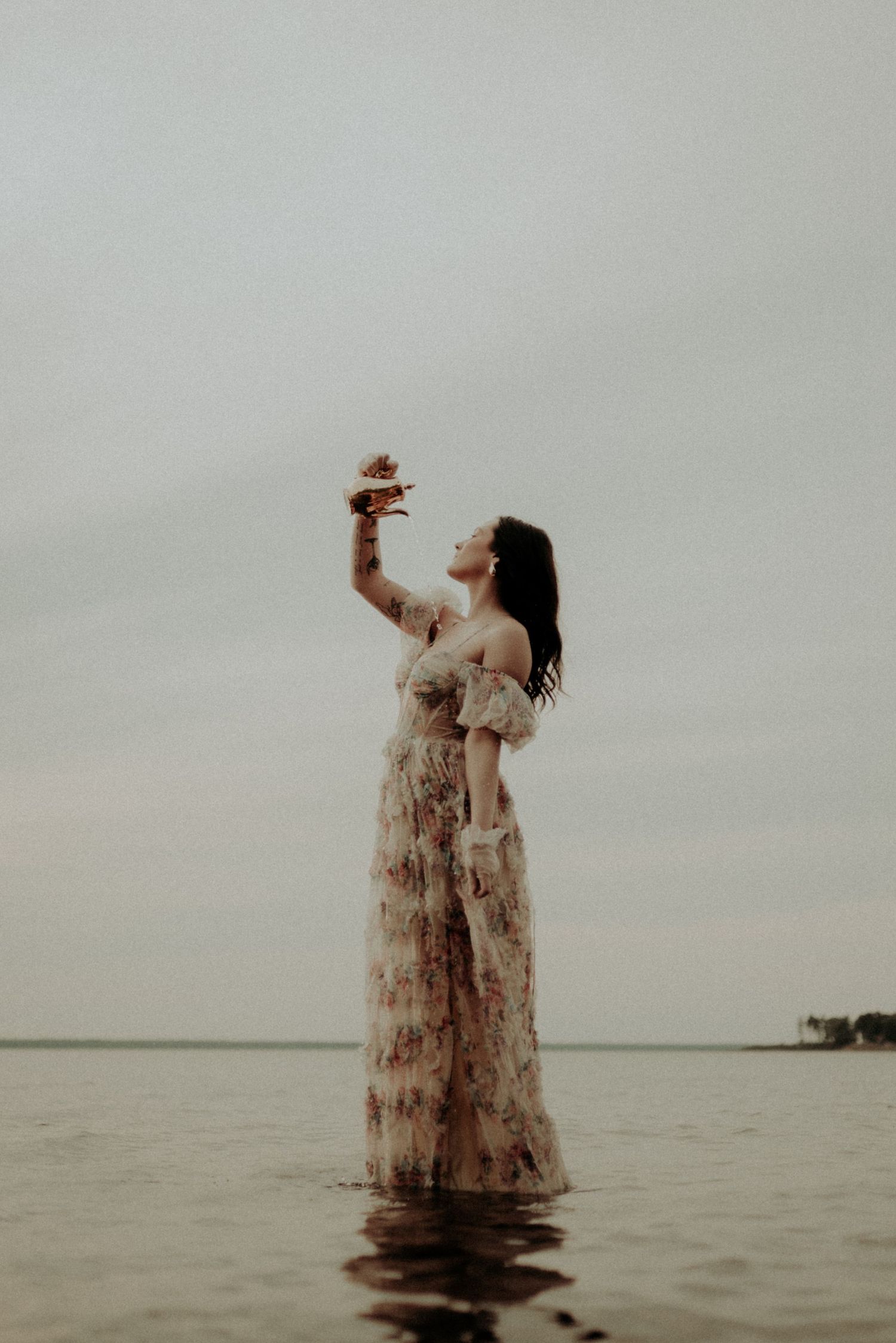 Artistic water portrait with figure in floral dress reaching upward at sunset.
