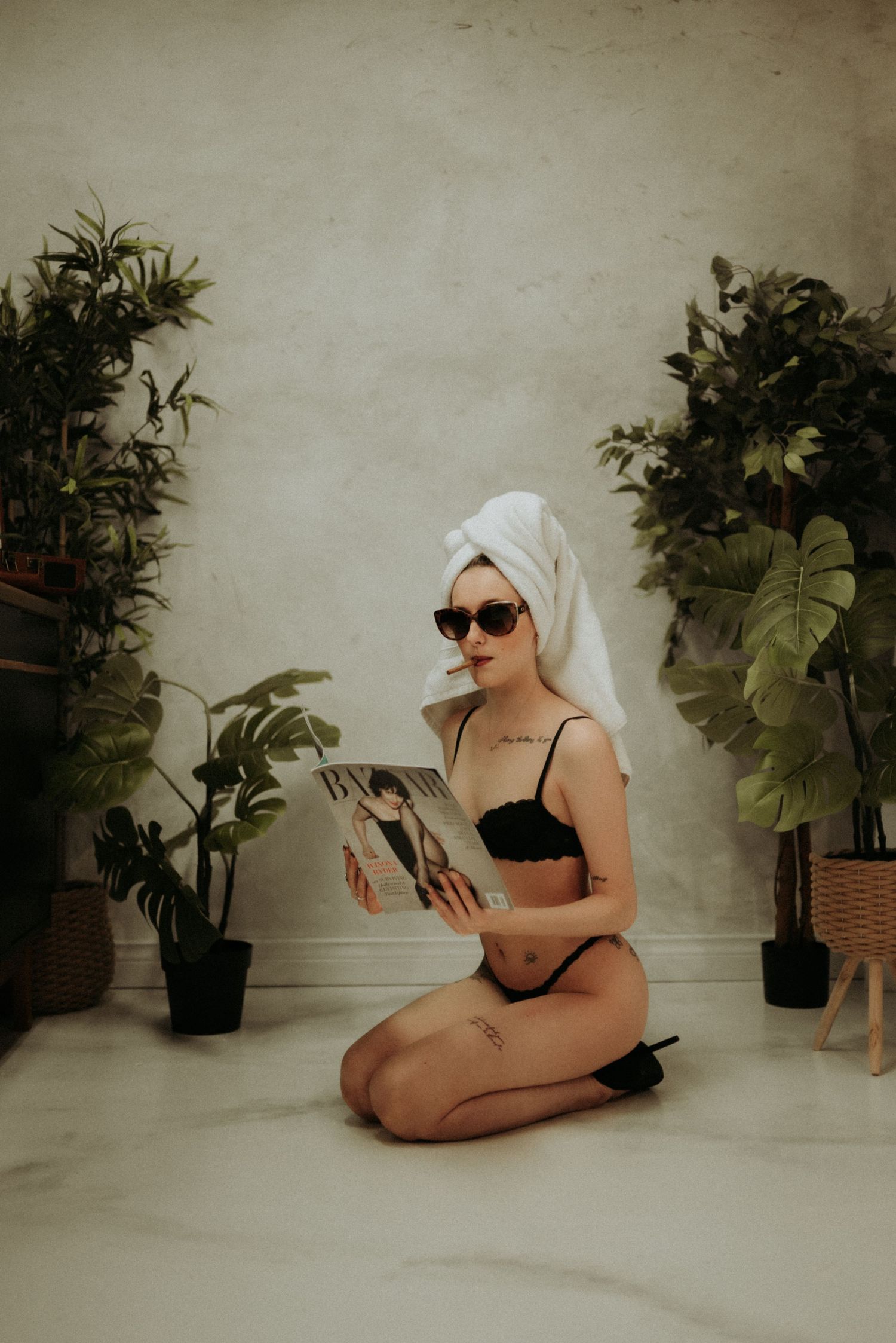 Artistic boudoir photo with retro styling featuring sunglasses, hair towel and potted plants.