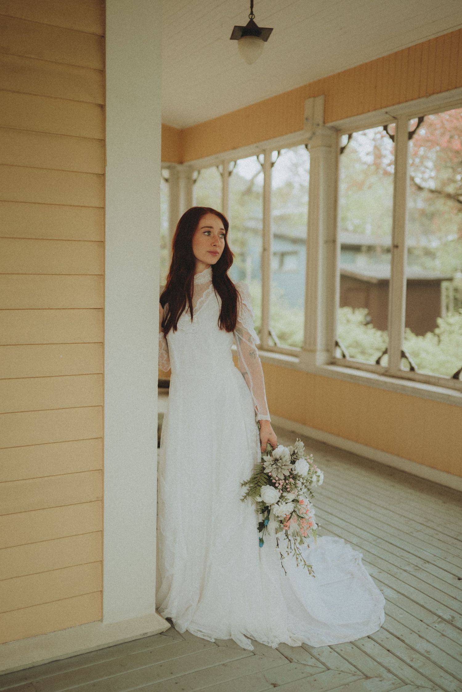 Wedding photography on a classic white porch featuring full-length lace gown and delicate bouquet.