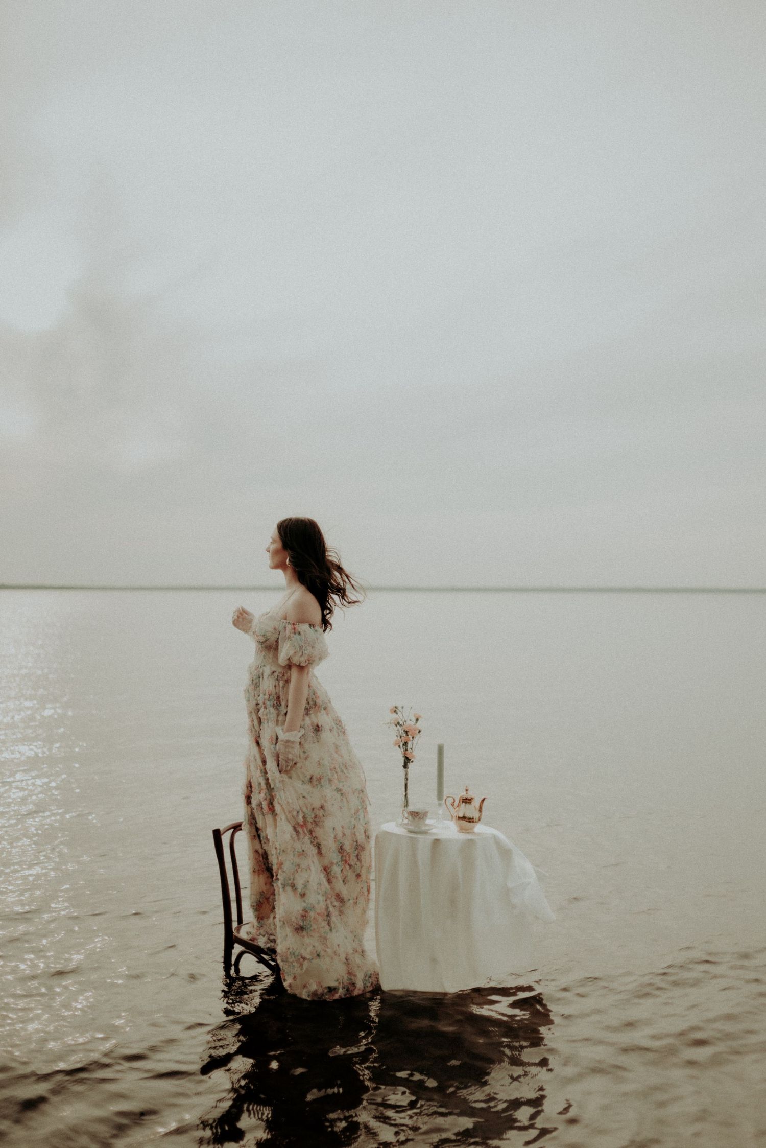 Whimsical water photography with flowing dress and romantic table setup against serene backdrop.
