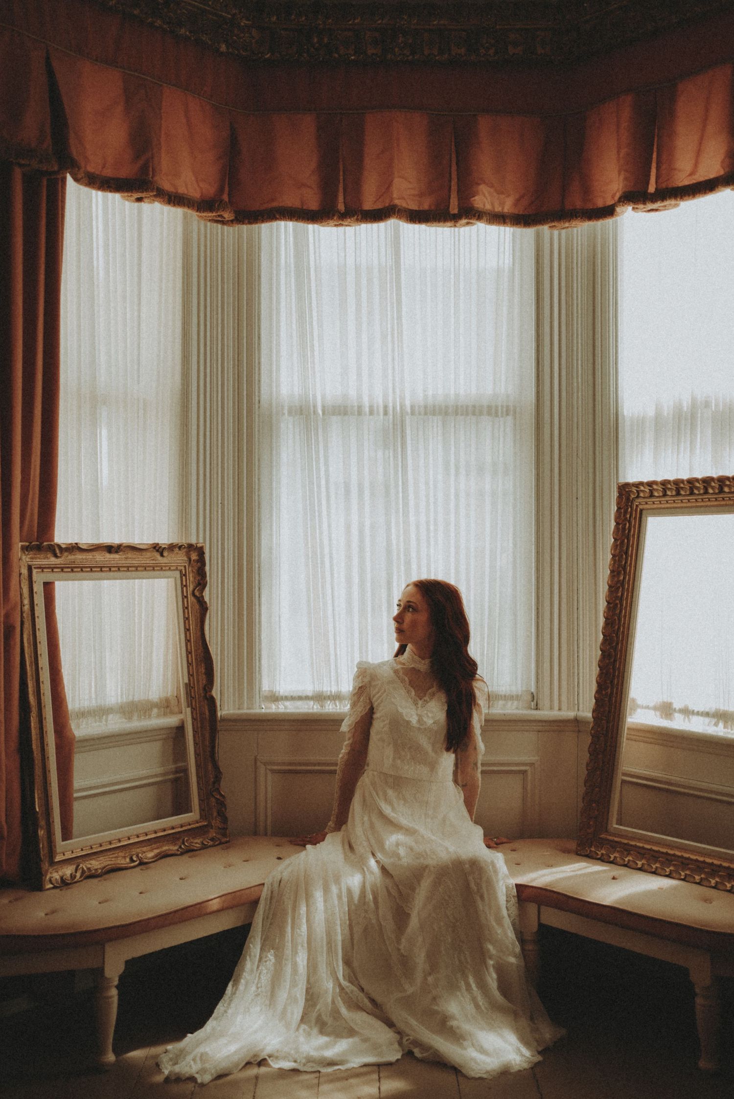 Ethereal bridal portrait series in a sunlit bay window with flowing white dress and dreamy atmosphere.